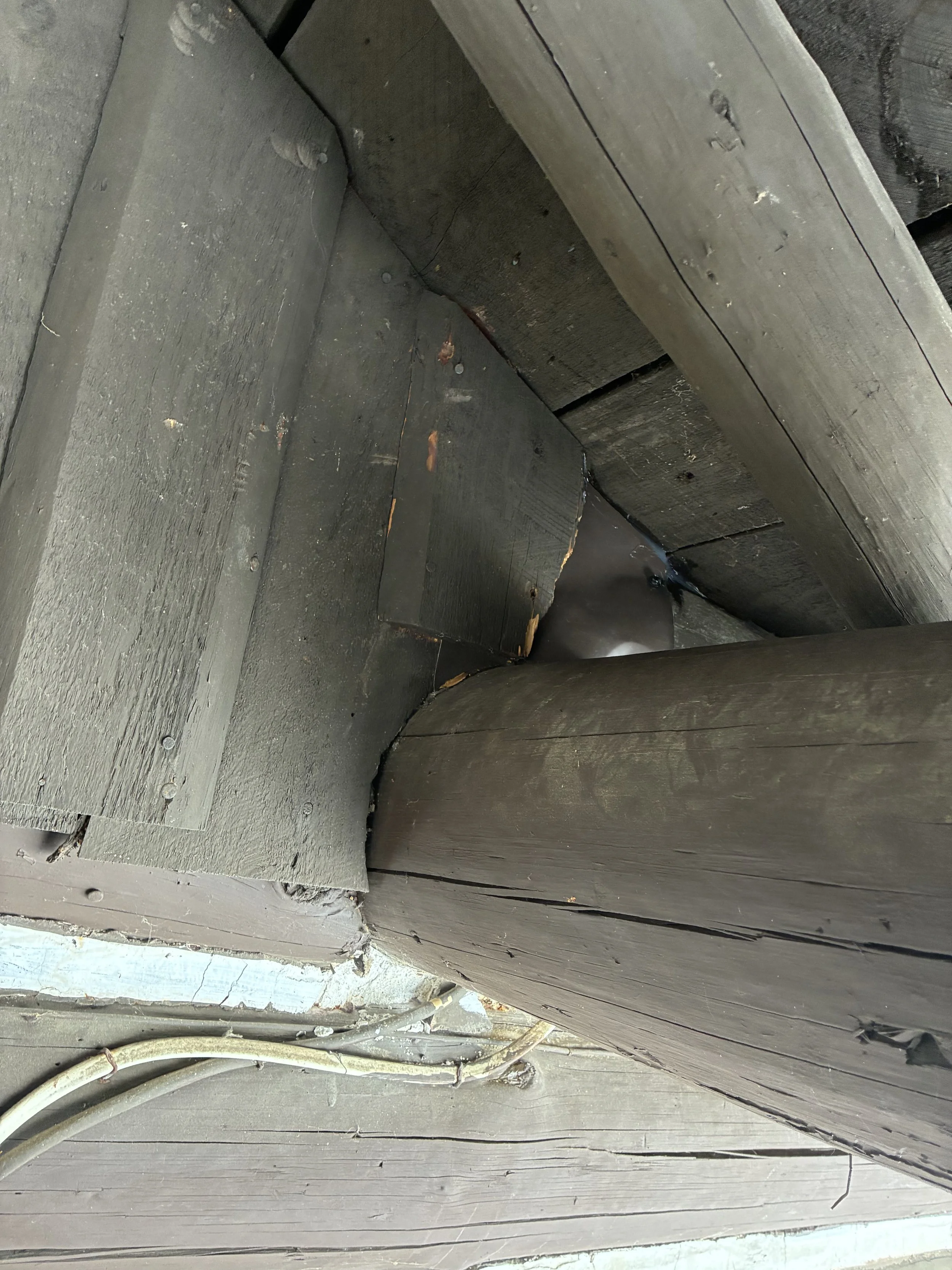 Close-up of weathered wooden house siding with visible nails and an electrical conduit at the bottom.