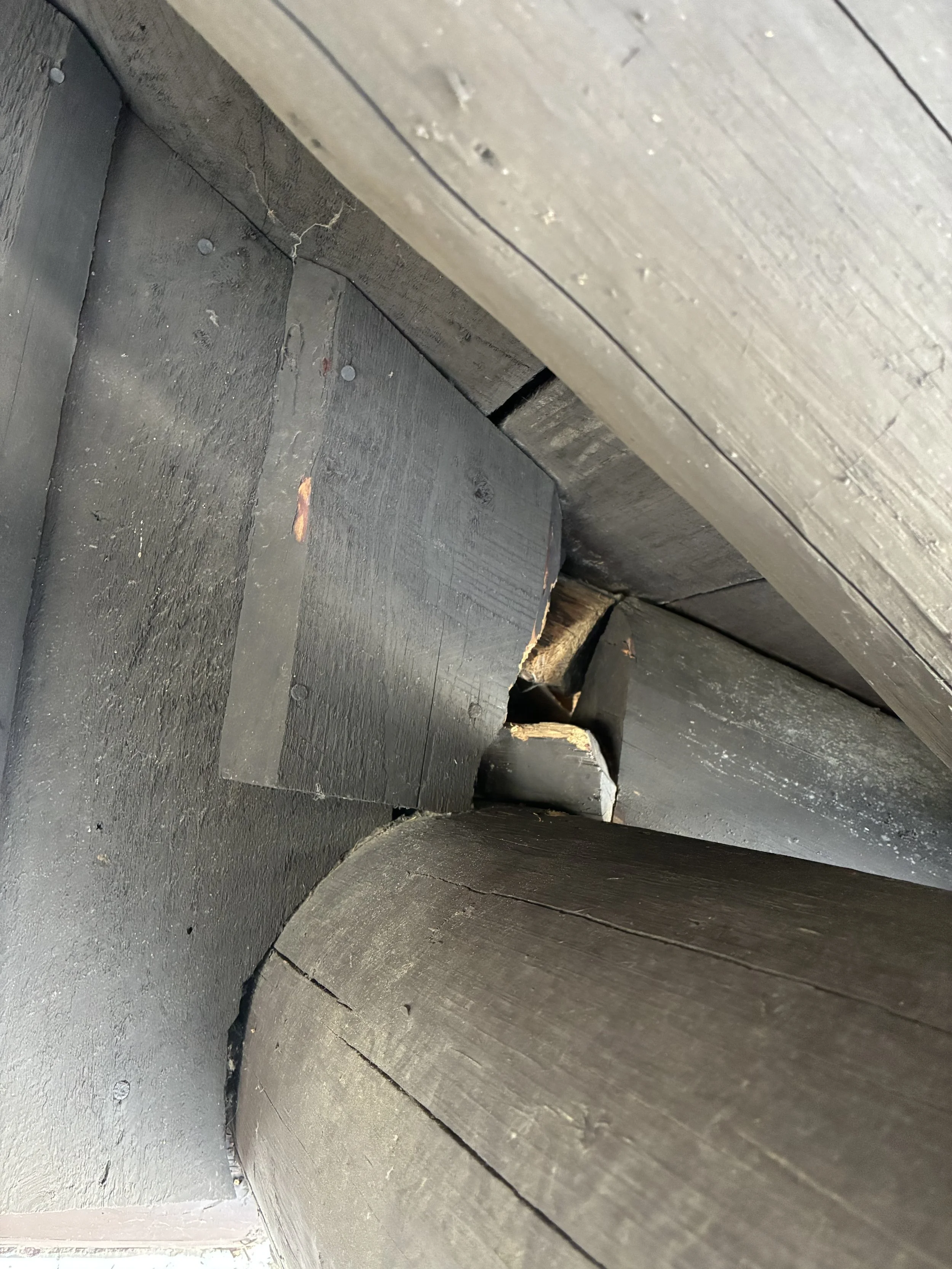 Close-up photo of stacked black wooden beams or planks, with visible grain, knots, and rough edges, showing construction or woodworking.