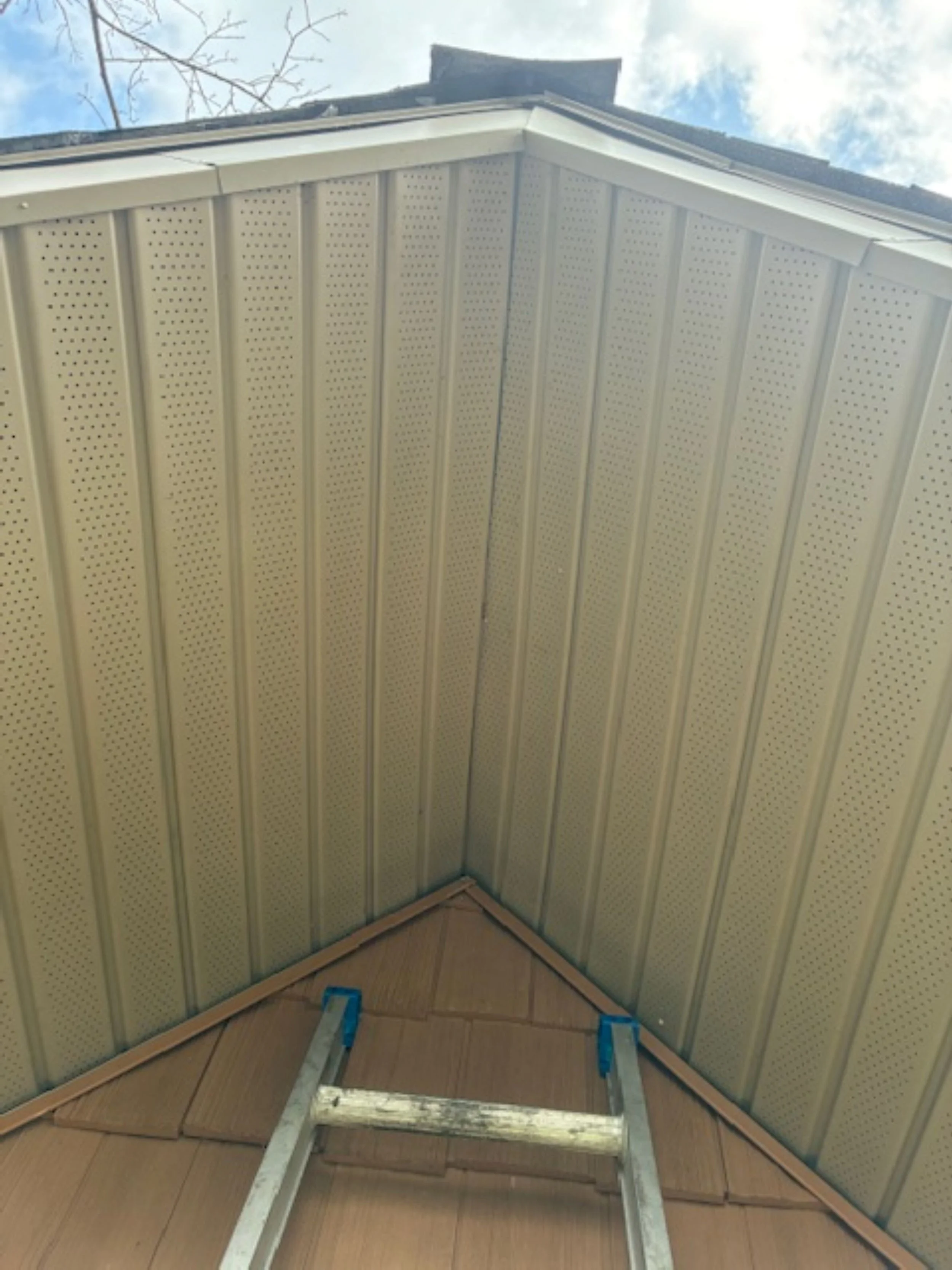 Interior of an attic with wooden flooring, beige paneled walls, and a ceiling with white perforated panels; a small stepladder is placed near the corner.