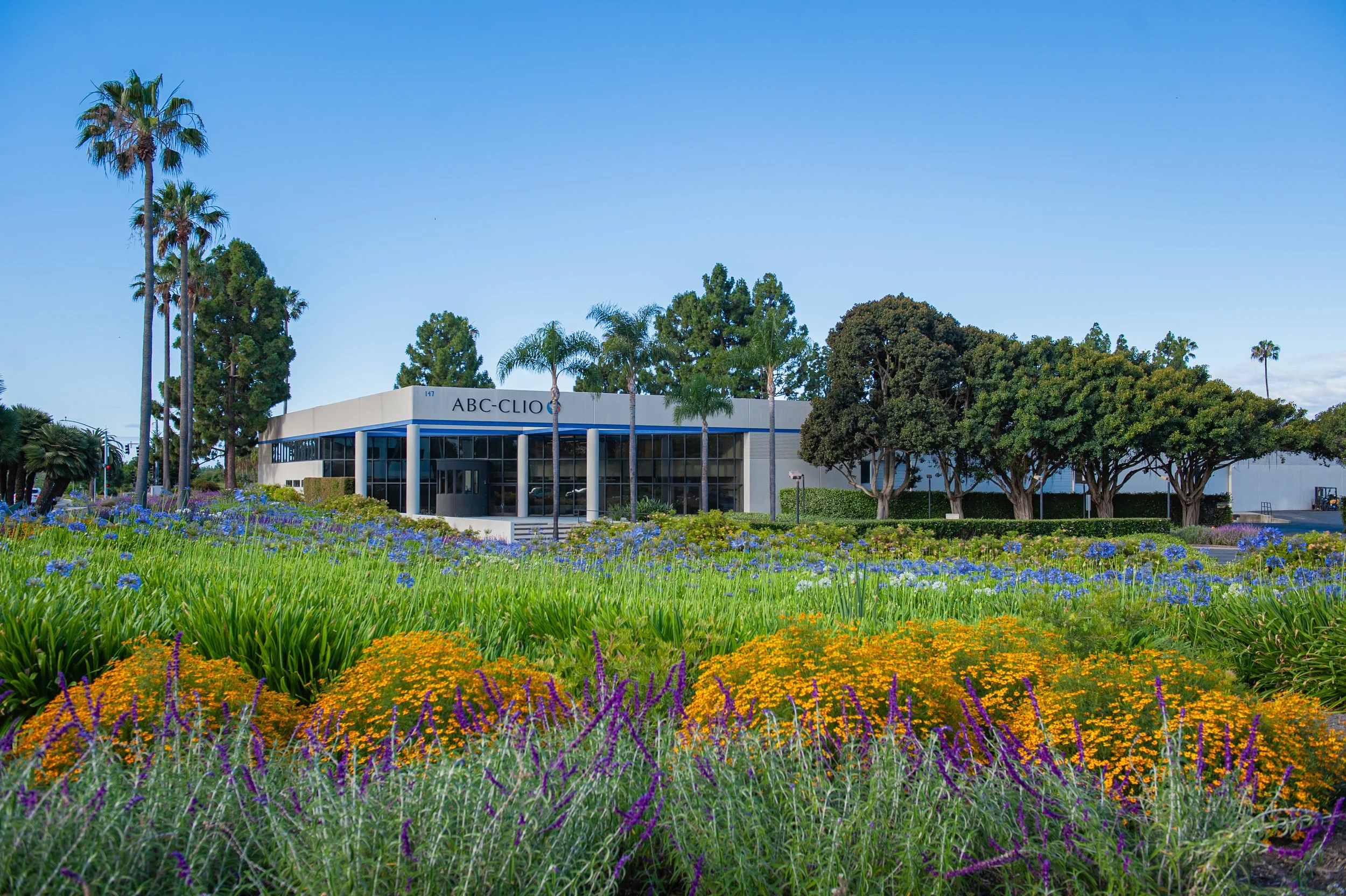 A commercial building surrounded by trees and colorful flowers and plants in the foreground.