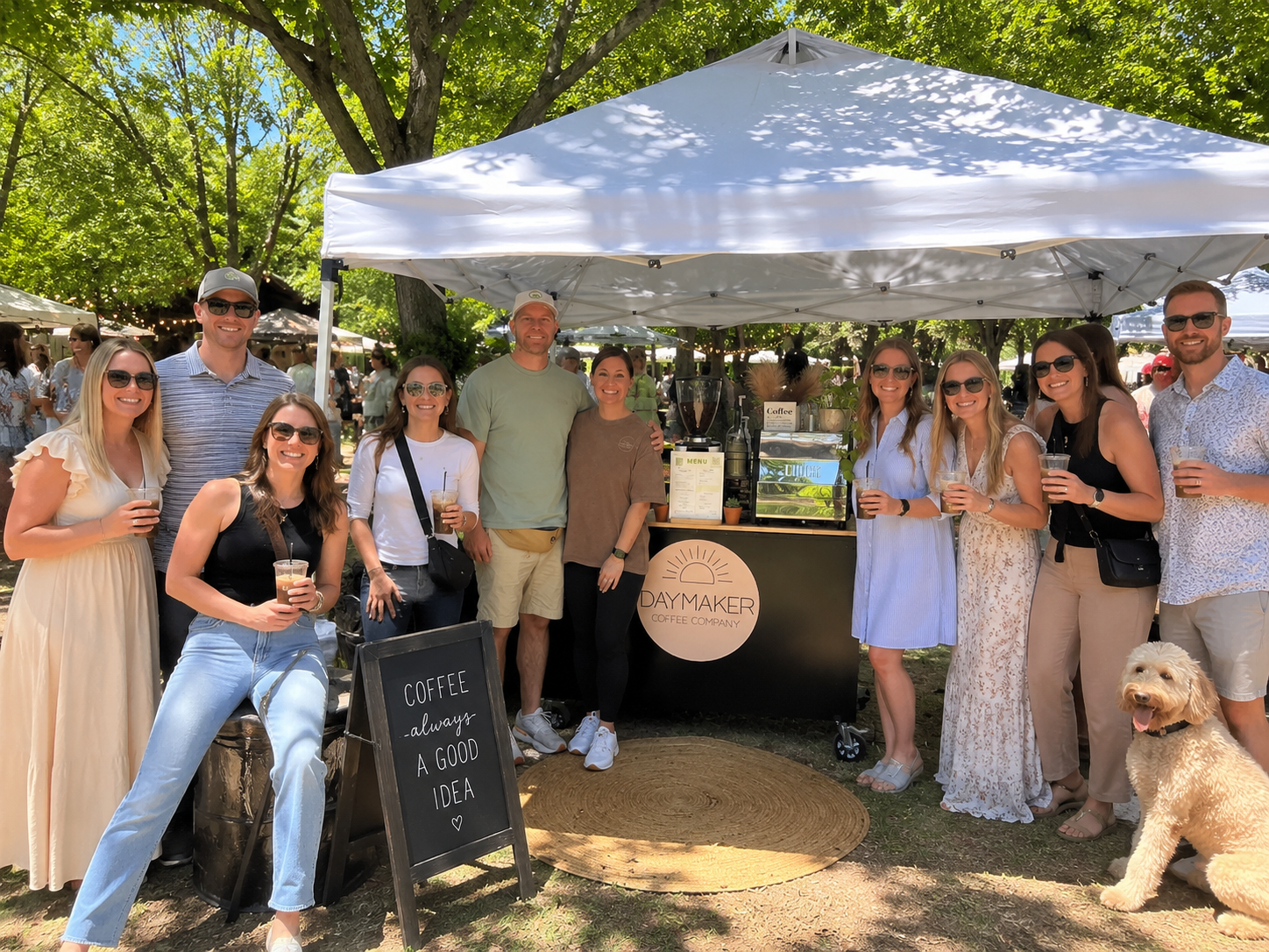 Guests smiling and enjoying drinks around the Daymaker Coffee Company mobile espresso cart at an outdoor event in Raleigh, NC