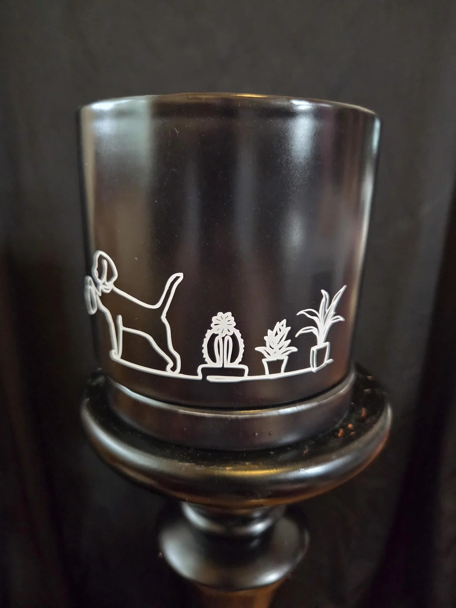 Black ceramic planter featuring a minimalist white line drawing of a dog watering plants, complete with a matching ceramic tray.