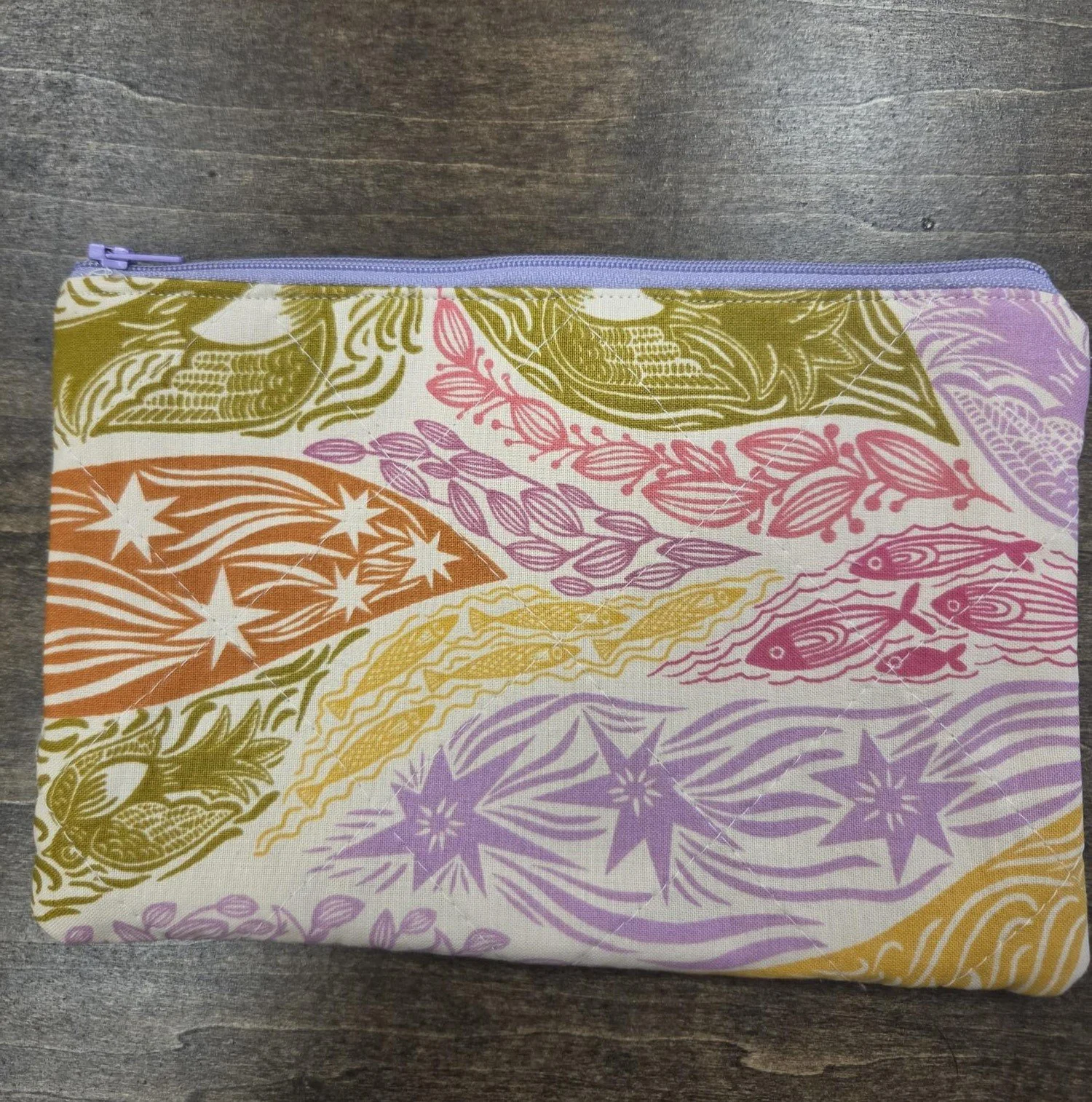 Handmade quilted cotton zipper pouch featuring a whimsical bohemian-inspired pattern in lavender, mustard, olive green, and coral with a coordinating lavender zipper.