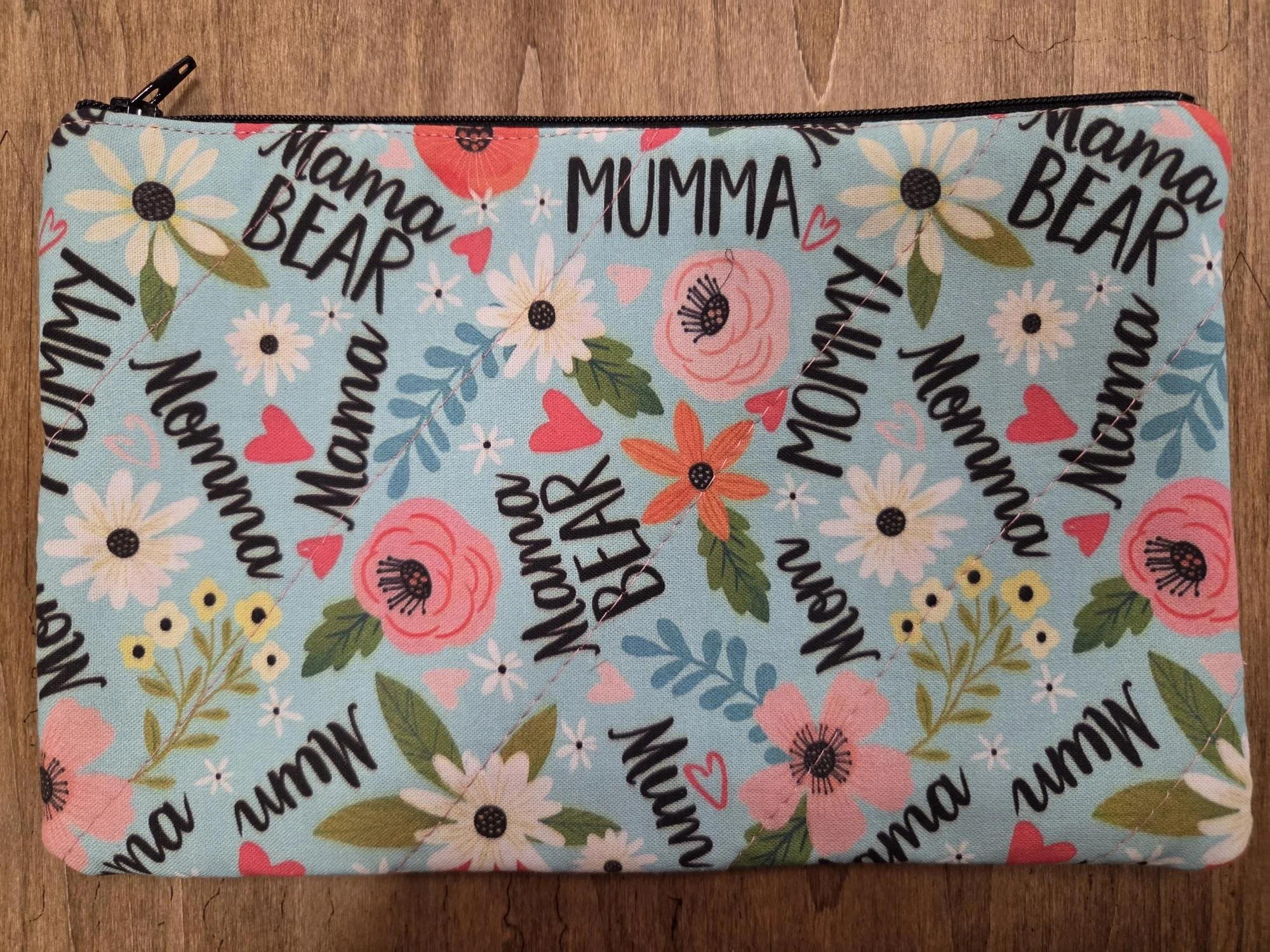 Handmade Mama Bear quilted zipper pouch with pink, coral and white flowers and hearts on aqua fabric with black zipper.