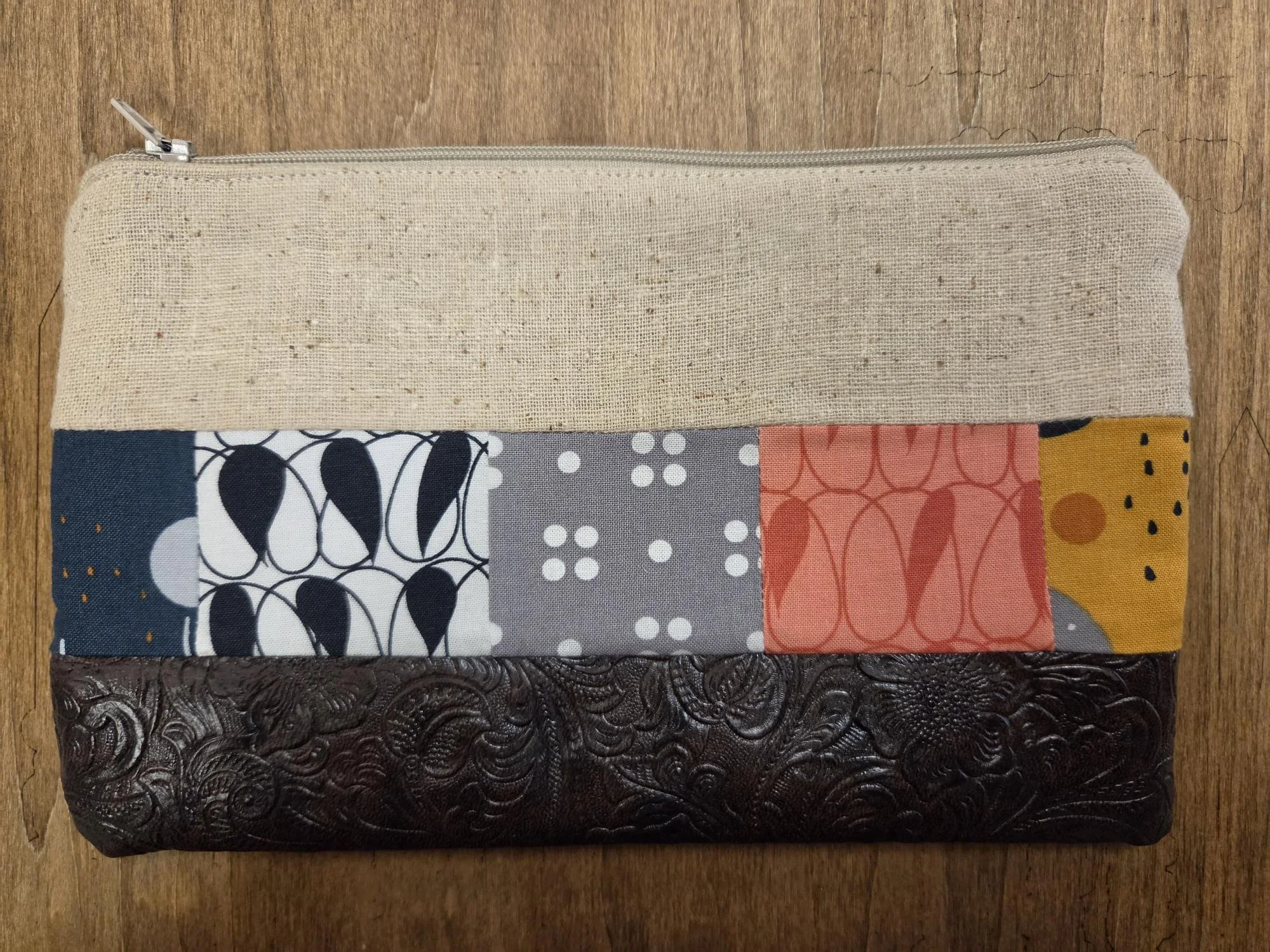 Handmade boho patchwork zipper pouch featuring natural linen fabric, colorful pieced cotton fabrics and embossed dark brown faux leather bottom.
