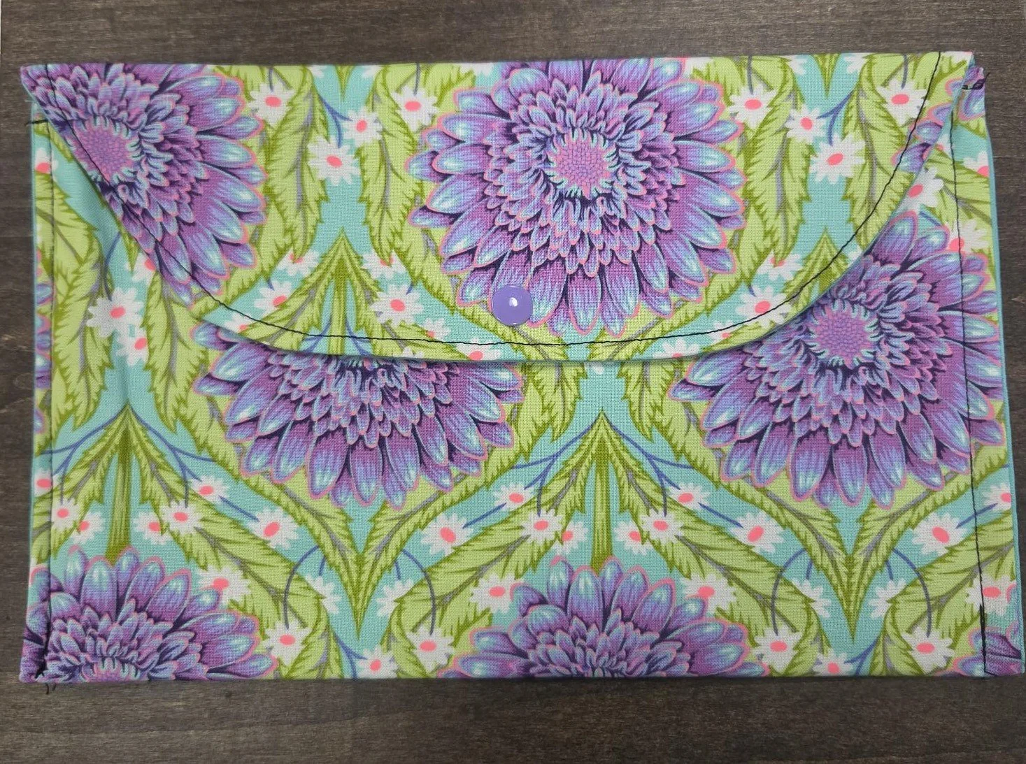 Handmade quilted small book sleeve featuring oversized lavender flowers on an aqua floral background with a snap closure, sized to fit most paperbacks and smaller hardback books.