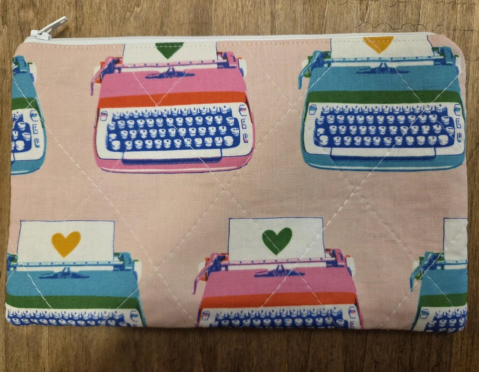 Handmade quilted zipper pouch with colorful pink, teal and blue retro typewriters and heart details on blush fabric.
