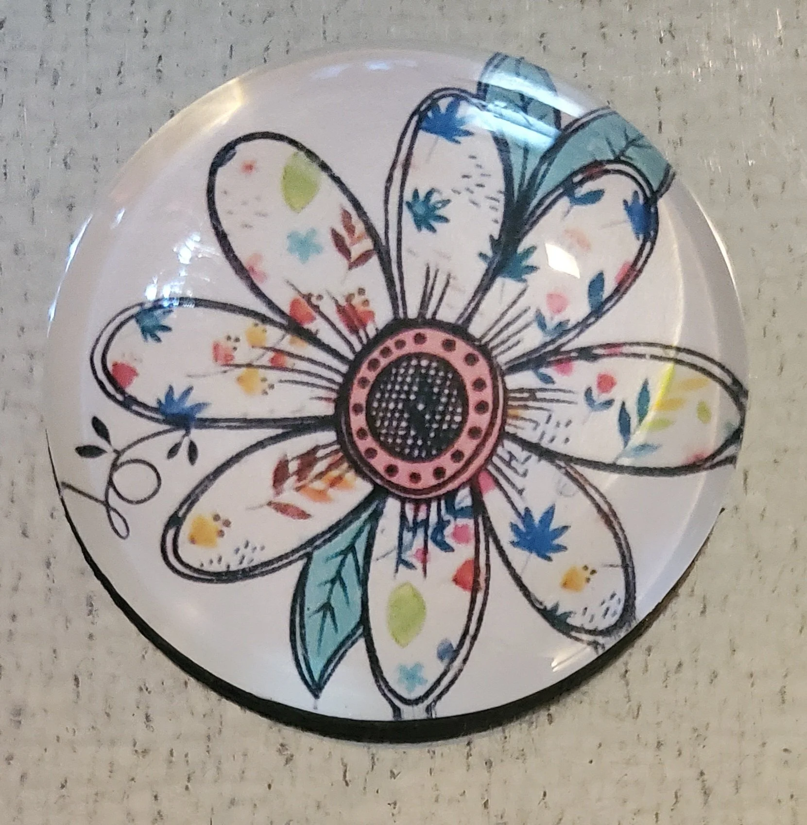 Handmade 2-inch round glass magnet featuring a whimsical hand-drawn wildflower with watercolor-style floral details beneath a crystal-clear glass dome.