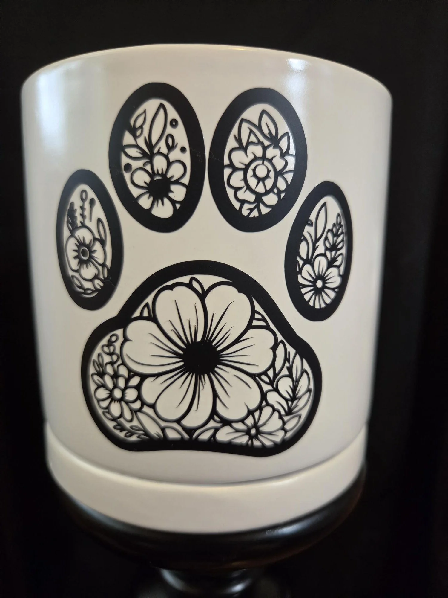 White ceramic planter featuring a black floral paw print design with matching saucer, perfect for pet lovers and indoor plants.