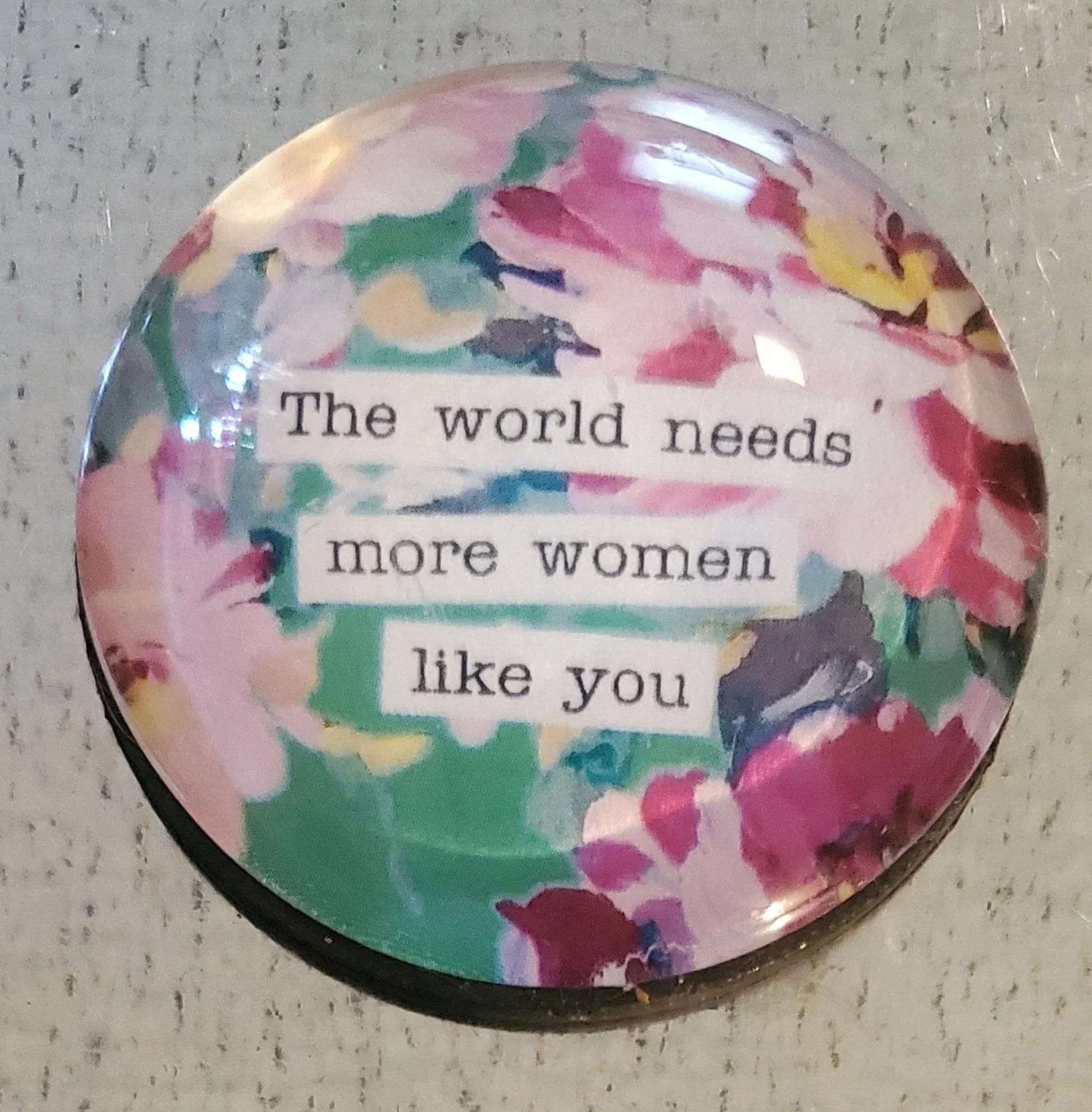 Handmade 2-inch round glass magnet featuring the quote "The world needs more women like you" on a colorful watercolor floral background.