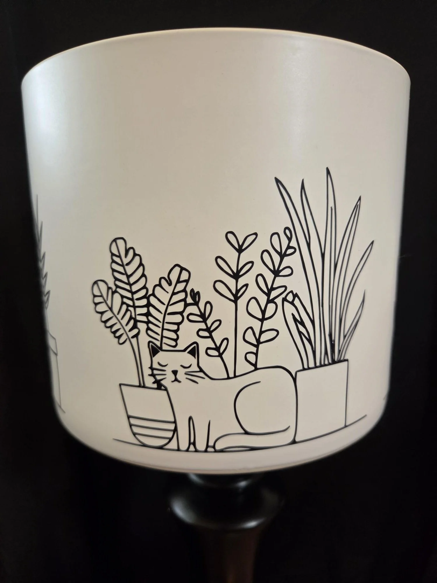 Large ceramic planter featuring four minimalist illustrations of sleeping cats surrounded by houseplants wrapped around the entire planter, available in black or white.