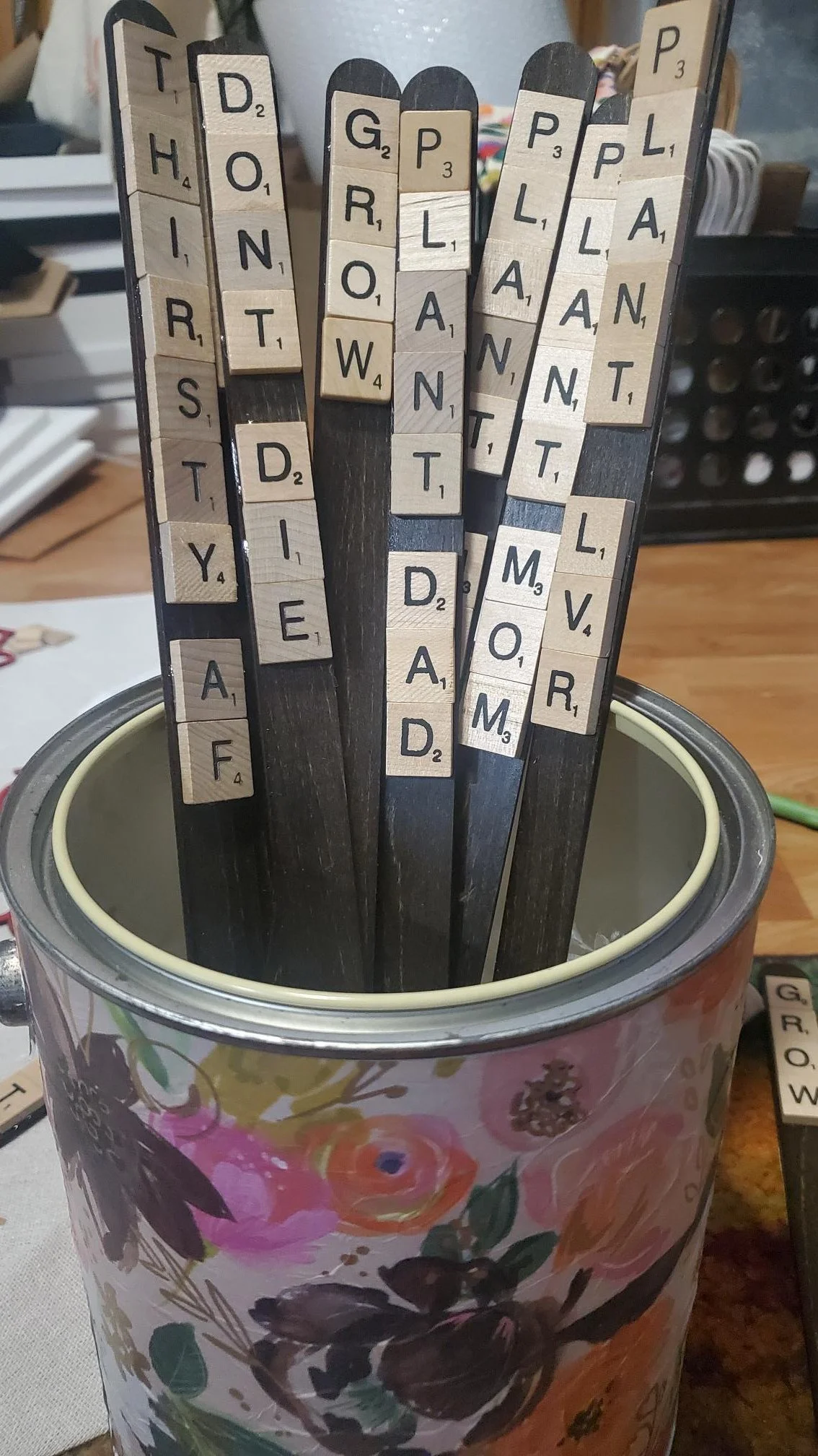 Handmade wooden plant stakes featuring authentic Scrabble tiles spelling funny sayings like "Soilmate," "Plant Mom," and "Soul Sis."