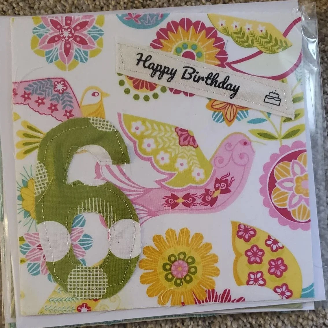 Handmade 6th birthday greeting card featuring a stitched green fabric number 6 on a colorful floral and bird patterned background with a Happy Birthday sentiment and decorative machine stitching.
