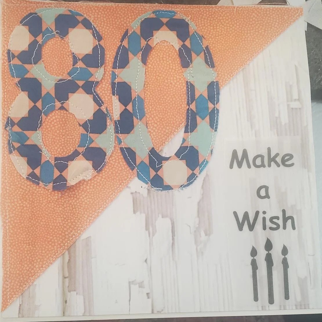 Handmade 80th birthday greeting card featuring stitched fabric numbers 80 on an orange geometric background with a "Make a Wish" birthday sentiment and decorative machine stitching.