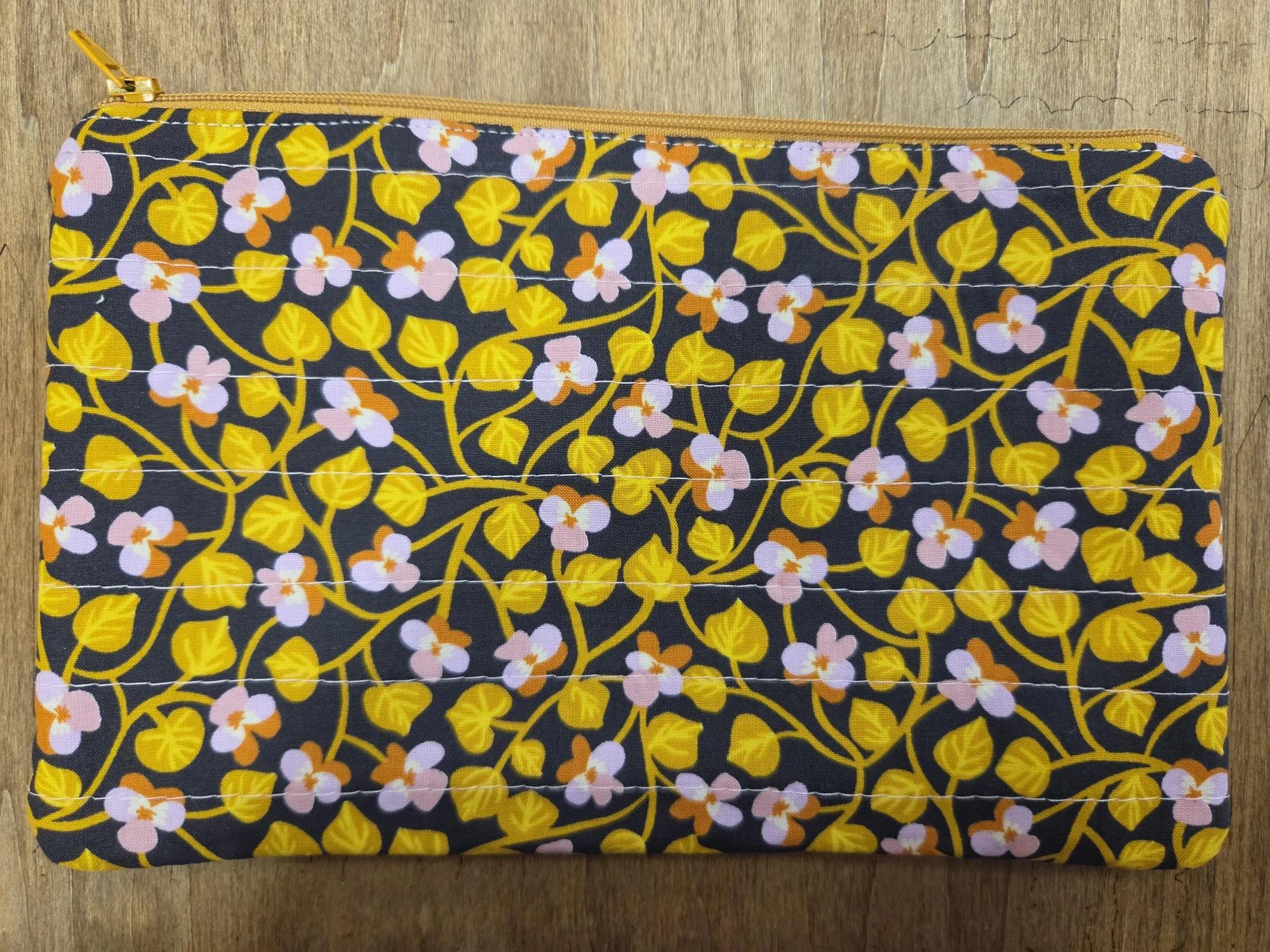 Handmade quilted zipper pouch with golden mustard vines and small blush pink flowers on deep navy fabric with coordinating gold zipper.