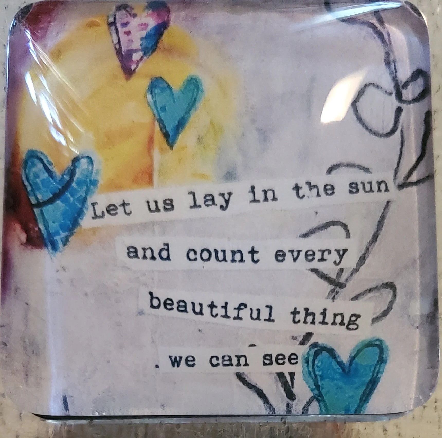 Handmade 2-inch crystal glass magnet featuring the inspirational quote "Let us lay in the sun and count every beautiful thing we can see" with blue hearts and soft mixed-media artwork.