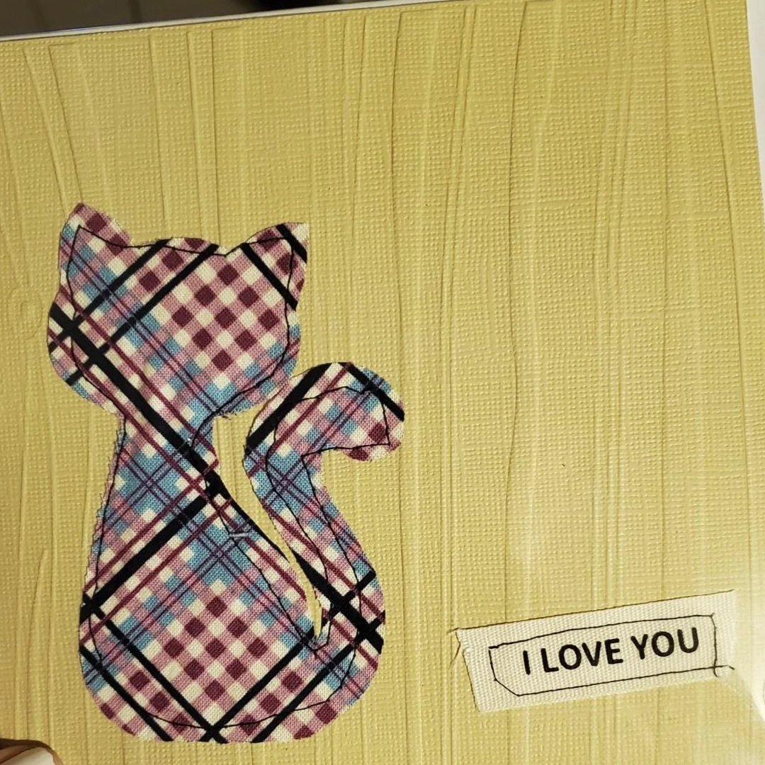 Handmade greeting card featuring a plaid fabric cat appliqué, textured yellow cardstock, decorative stitching, and an I Love You sentiment.