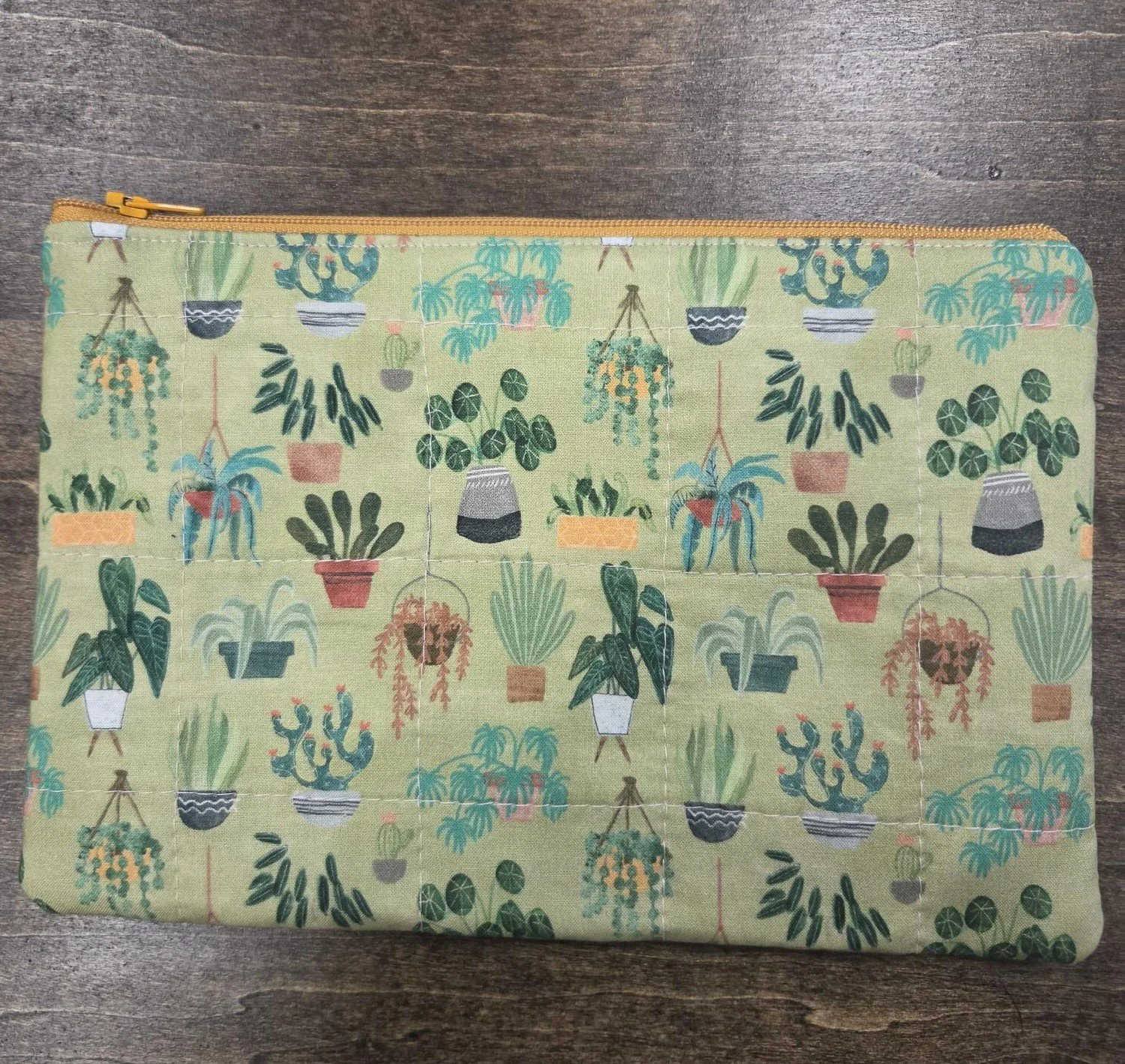 Handmade quilted cotton zipper pouch featuring colorful illustrations of houseplants, hanging baskets, succulents, and potted plants on a soft sage green background with a coordinating mustard zipper.