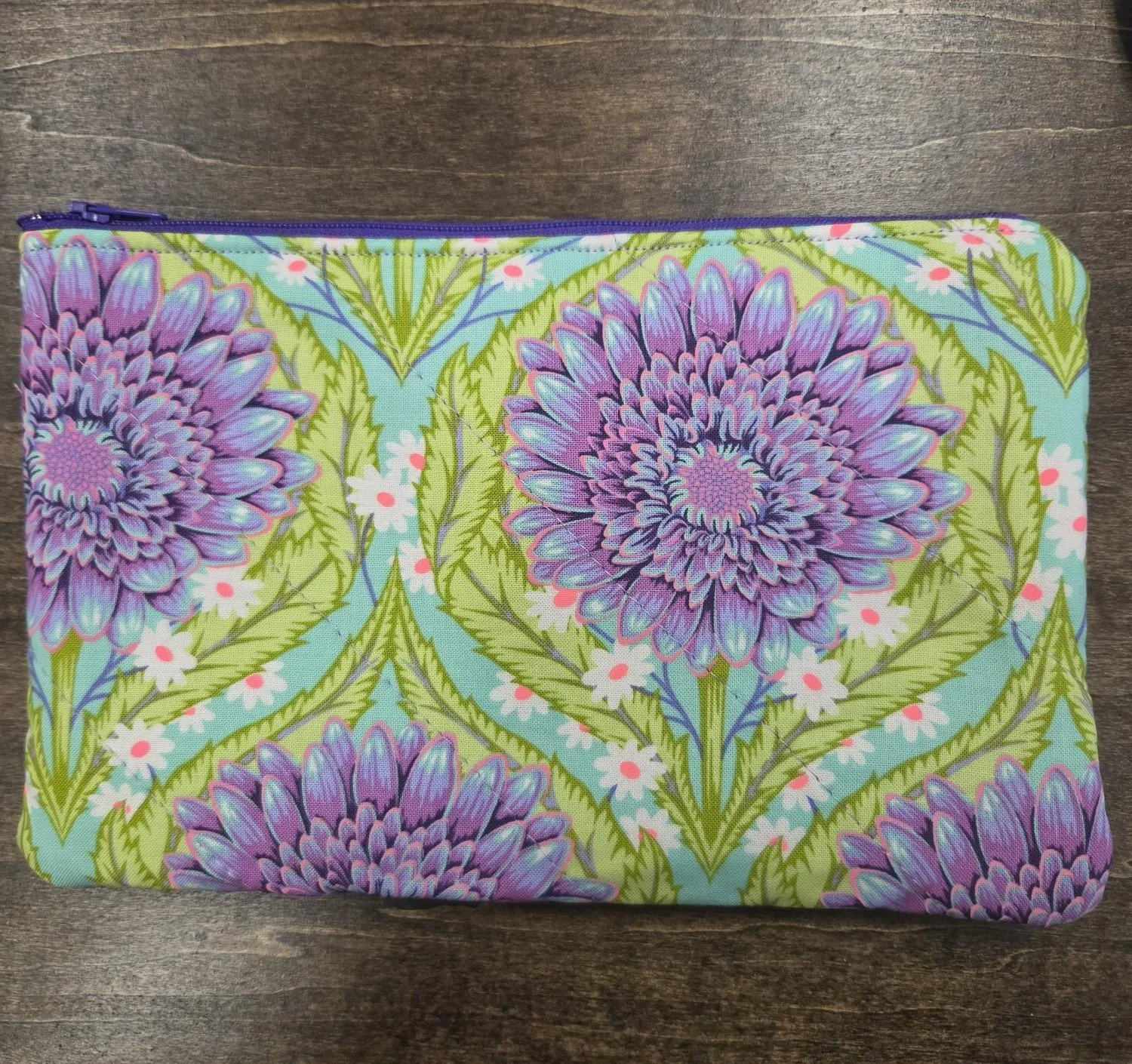Handmade quilted zipper pouch featuring large purple flowers on aqua cotton fabric with green leaves and a coordinating purple zipper.