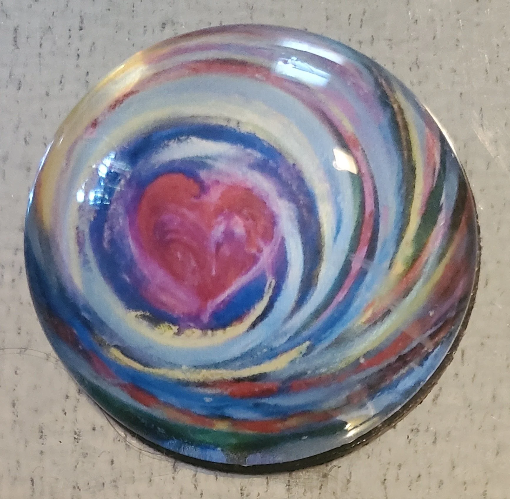 Handmade 2-inch round glass magnet featuring a colorful abstract watercolor heart surrounded by swirling blue, pink, purple, and teal brushstrokes beneath a crystal-clear glass dome.