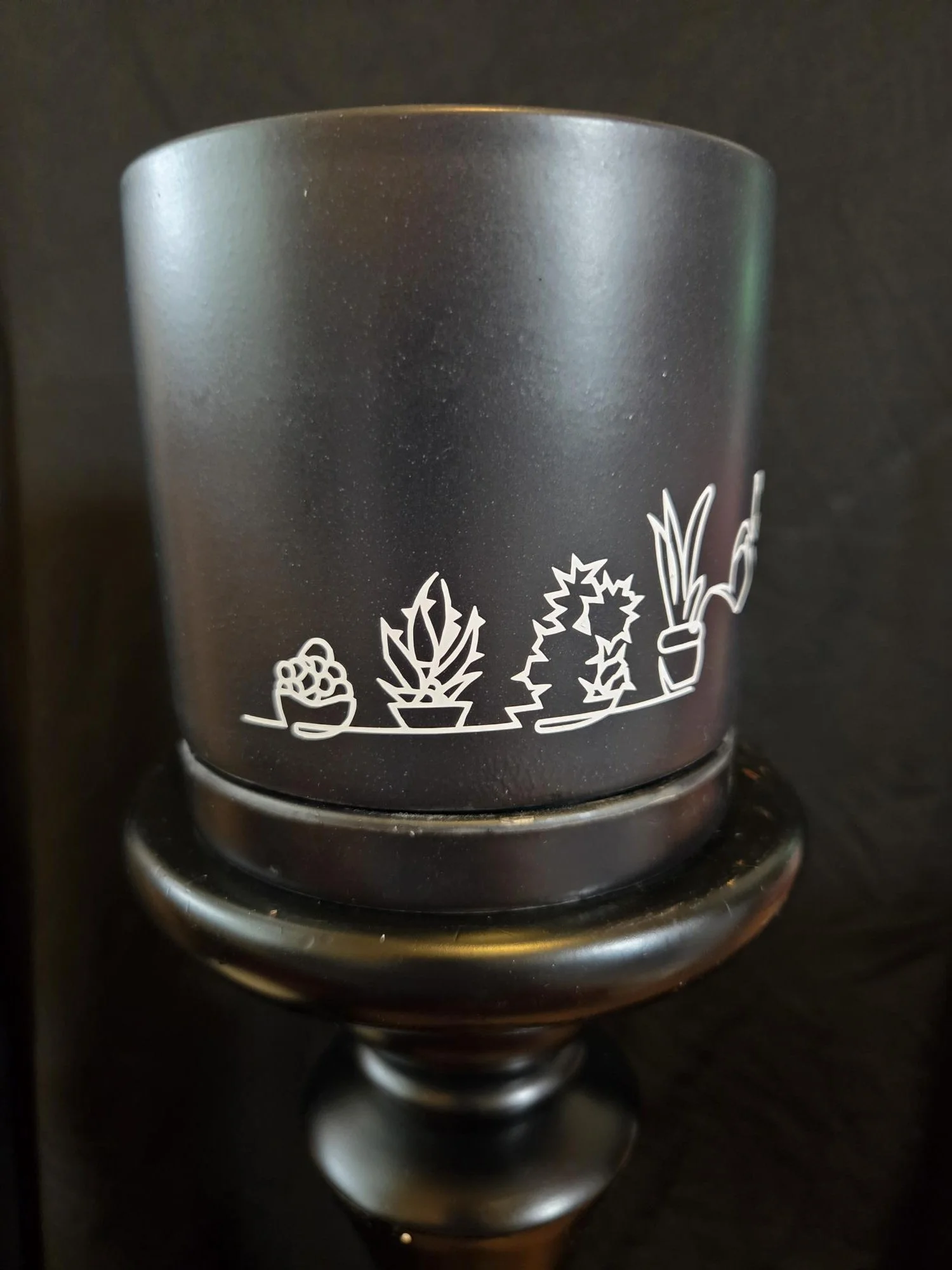 Black ceramic planter featuring a minimalist white line drawing of a cat watering plants, complete with a matching ceramic tray.