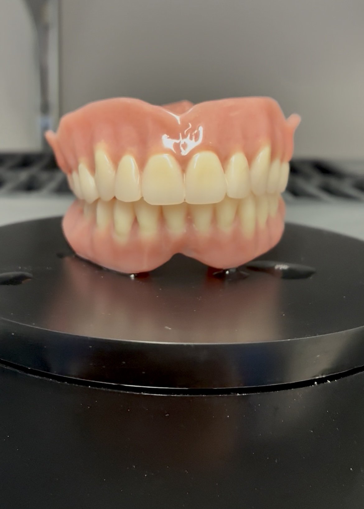 A set of artificial teeth with pink gums resting on a reflective black surface.