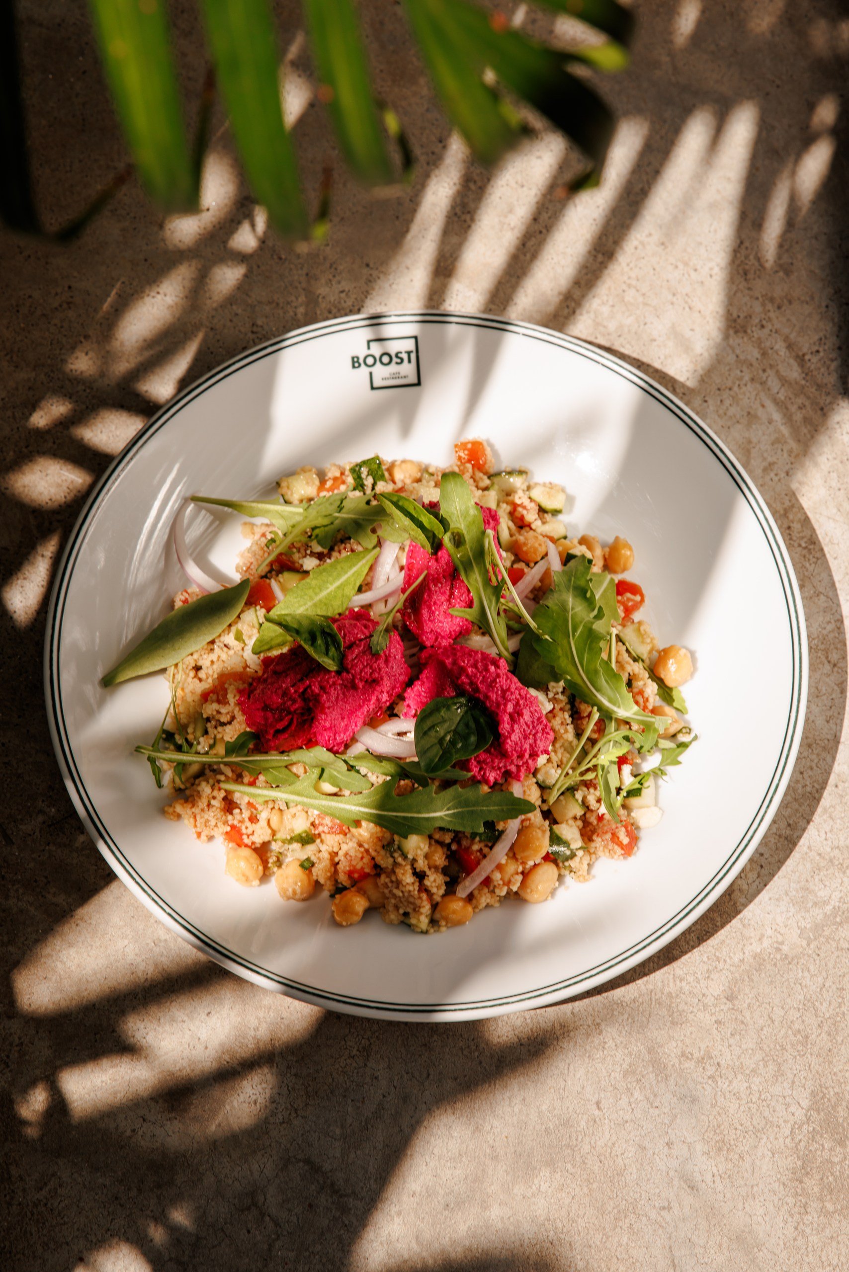 A plate of colorful salad with greens, chickpeas, and red beet slices on a table with shadows of leaves above.