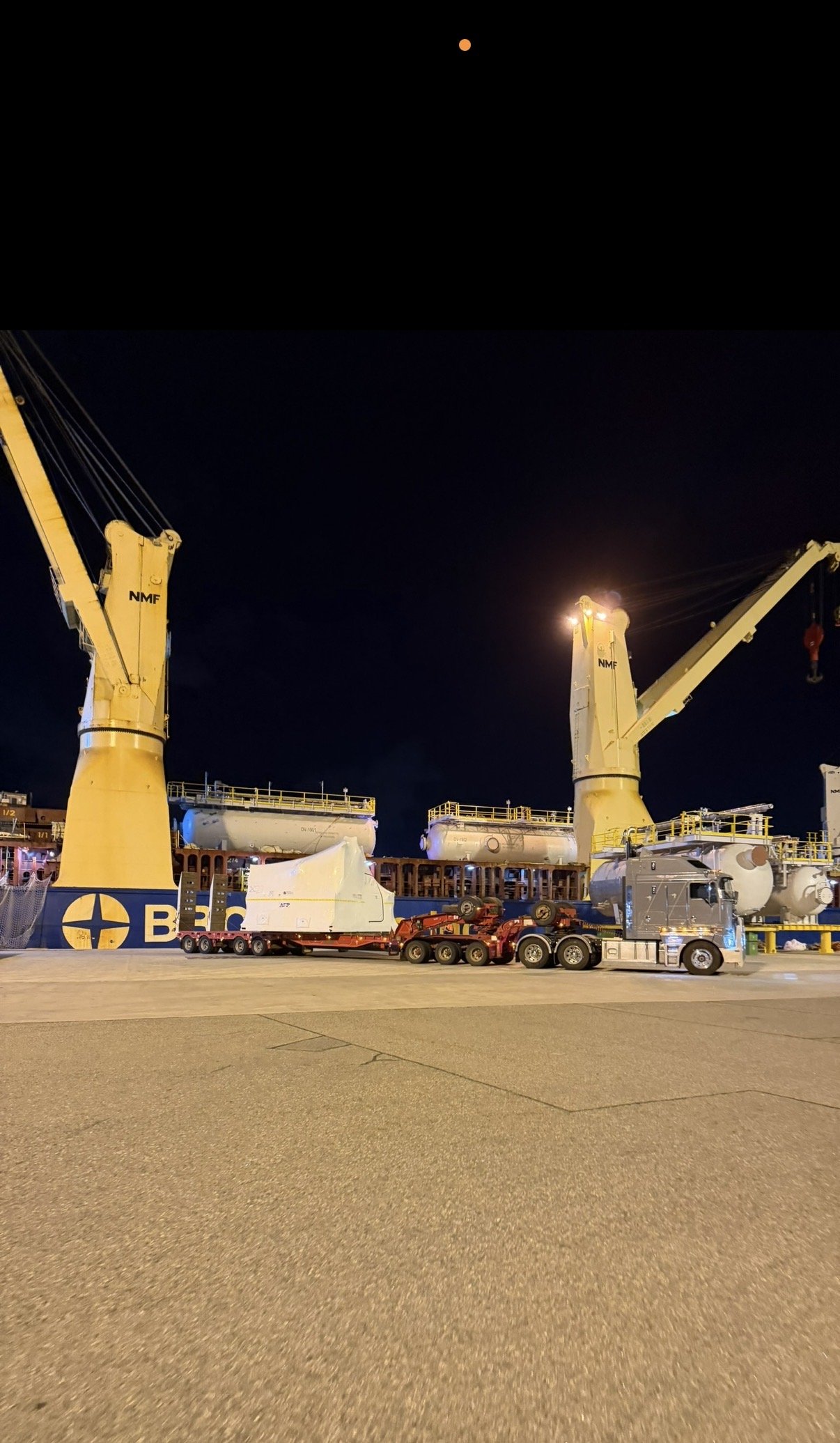 Nighttime scene at an airport or shipyard with large yellow cranes, trucks, and equipment on the tarmac, under a dark sky with a bright orange moon.