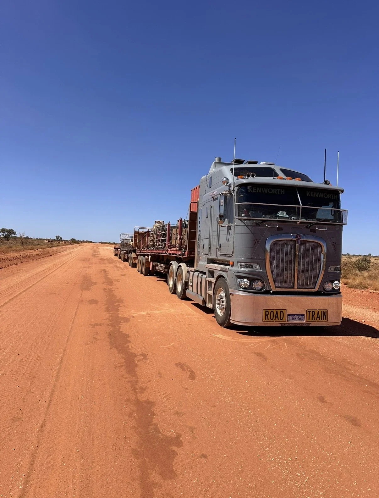 A large semi-truck parked on a dirt road in a desert landscape with a clear blue sky.