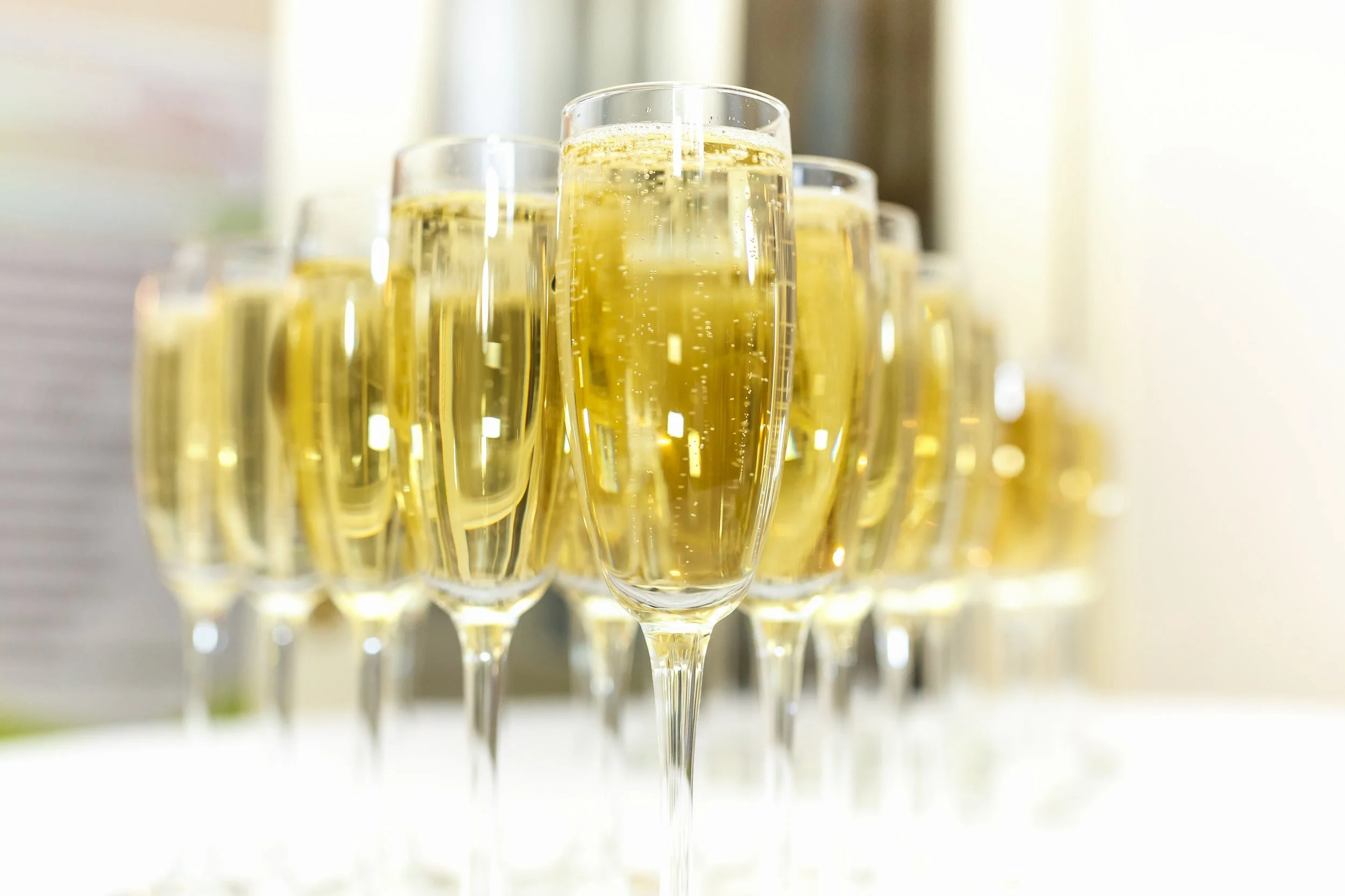 Multiple glasses of champagne on a reflective surface, with a blurred background.