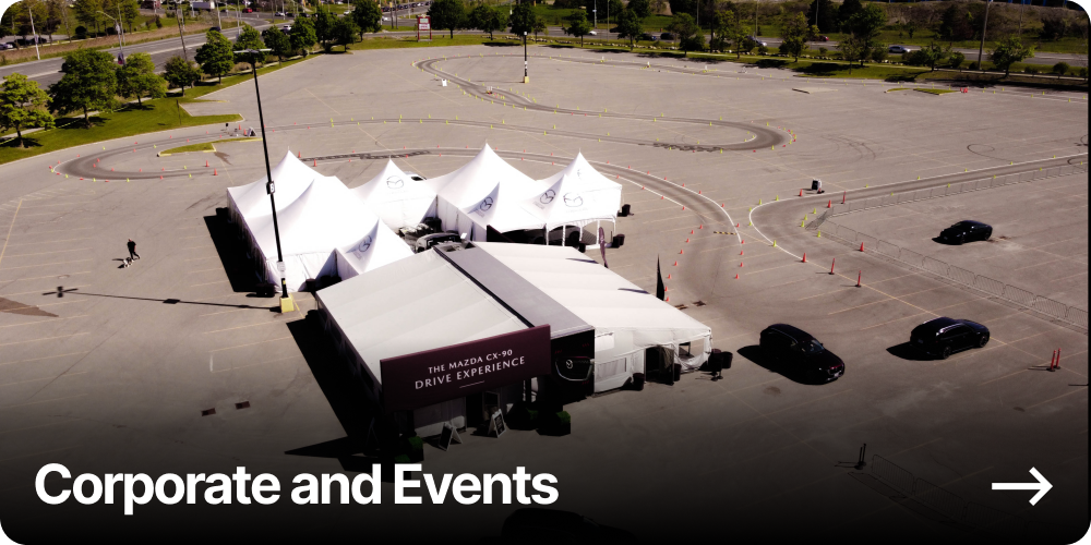 Large outdoor tent setup in a mostly empty parking lot with cars and driving course marked with traffic cones.