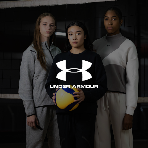 Three women in athletic apparel stand together on a volleyball court, with the woman in the center holding a volleyball and the Under Armour logo overlayed in front.