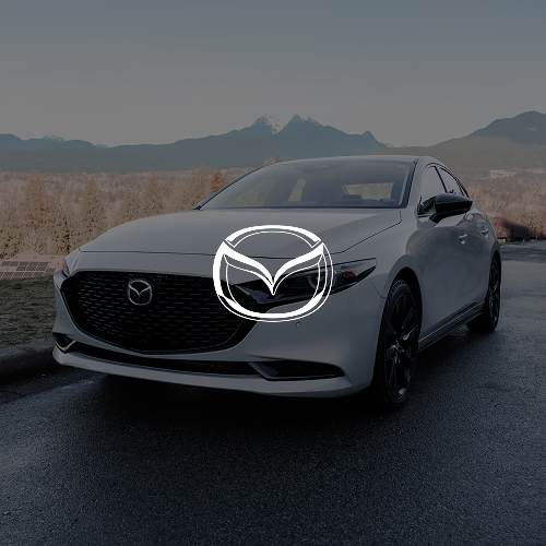 A silver Mazda sedan parked on a road with mountains in the background.