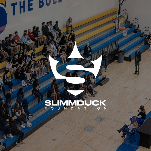 A gymnasium filled with students sitting on bleachers, with a few standing and a basketball hoop visible in the background. The SLIMMDUCK Foundation logo is superimposed in the center.