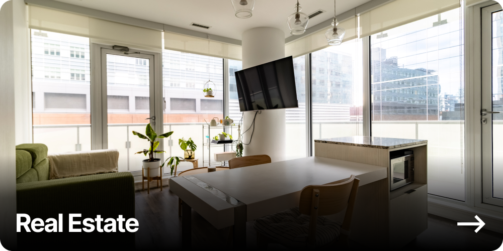 Bright modern apartment living area with large windows, green sofa, plants, mounted TV, and dining table.