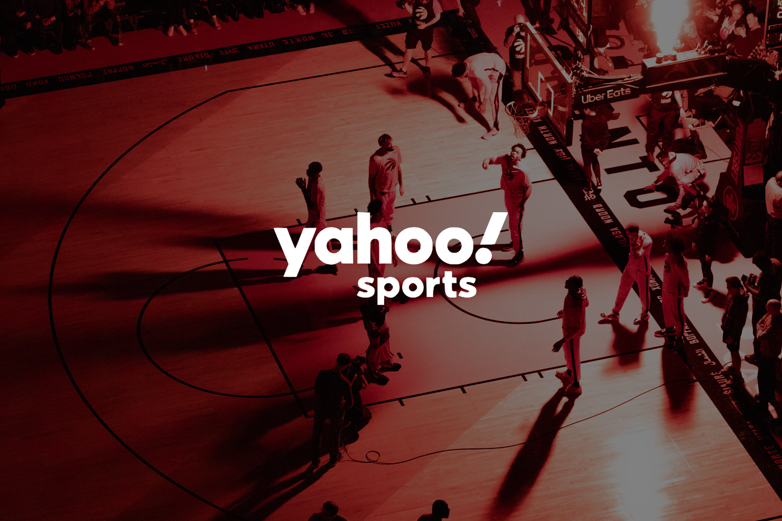 An aerial view of a basketball game with players on the court, spectators seated along the sides, and the Yahoo Sports logo overlaid on the image.