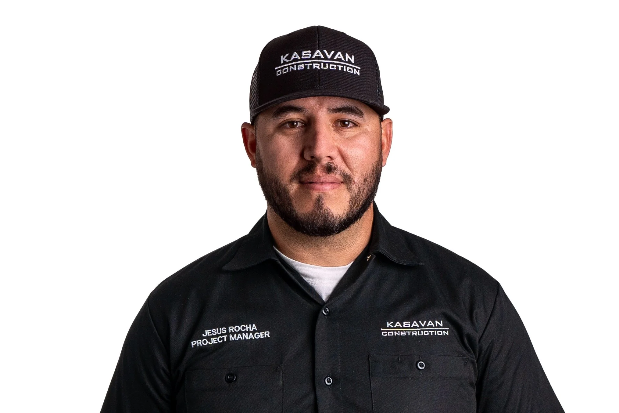 A man with a beard wearing a black Kasavan Construction uniform and a black cap with Kasavan Construction logo, against a white background.