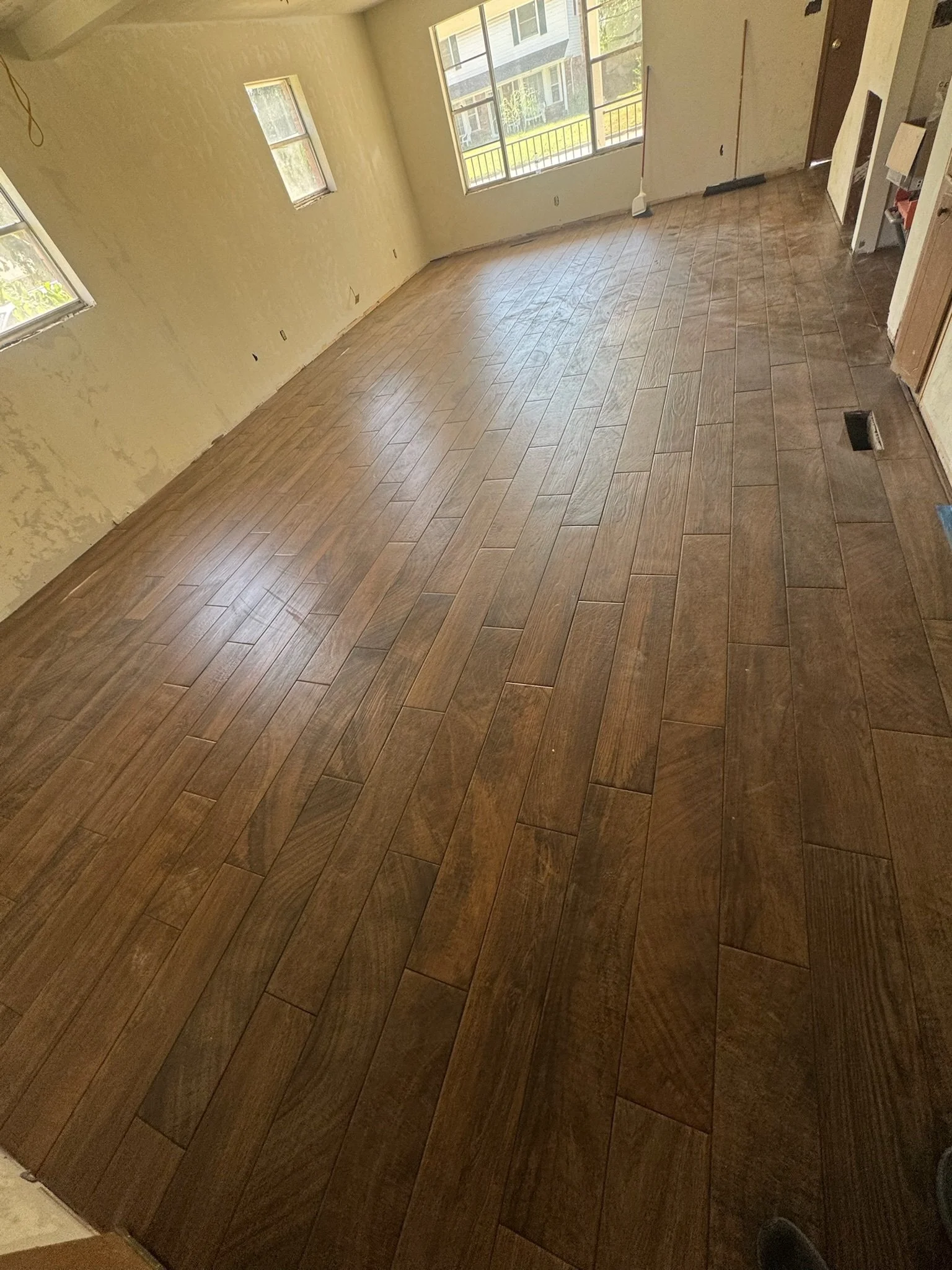 Room with wooden tile flooring, windows, and partially finished walls, likely under renovation.