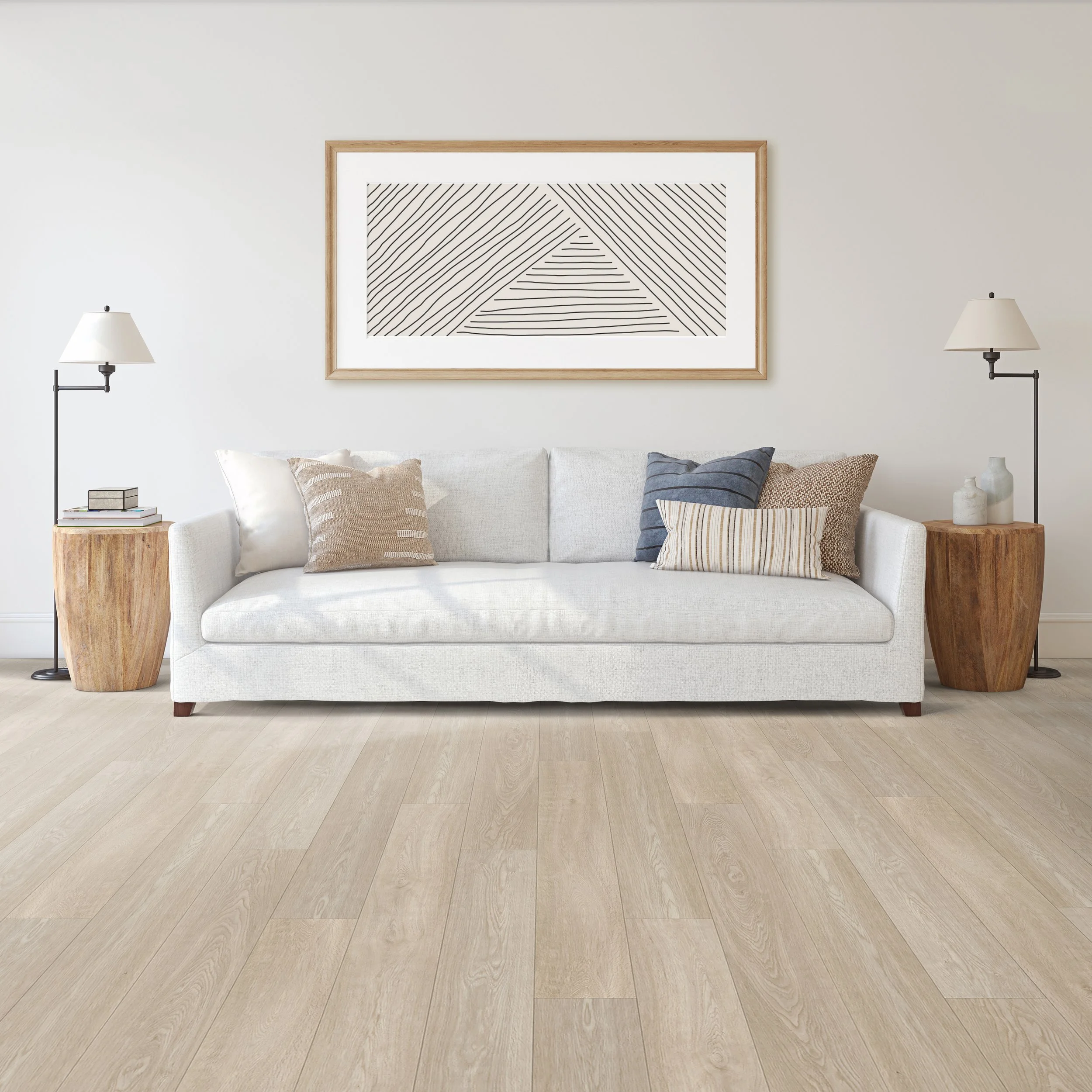 Living room with a white sofa, beige and blue throw pillows, two wooden side tables, and two wall-mounted lamps, with a large framed black and white geometric art piece on a white wall, and light-colored wood flooring.