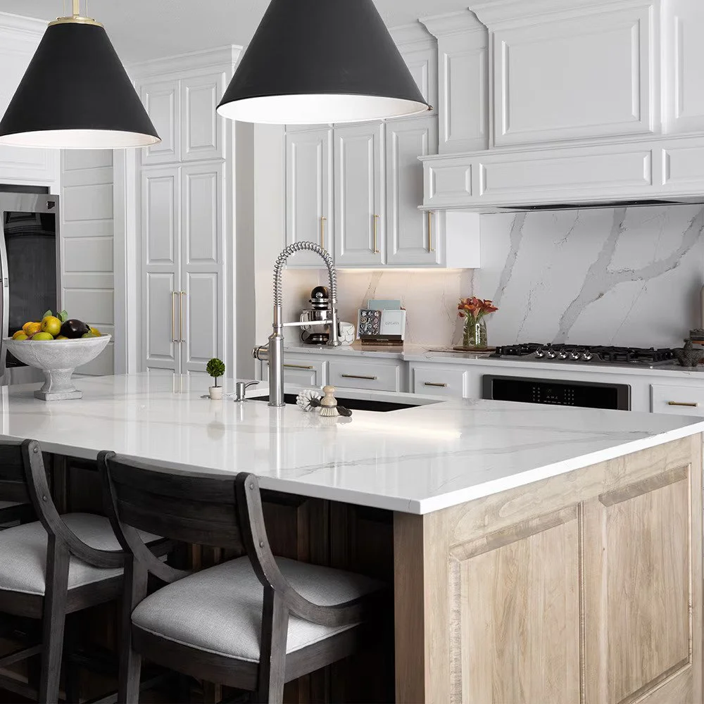 Modern kitchen with white cabinetry, marble backsplash, black pendant lights, and a white countertop island with dark wooden chairs.