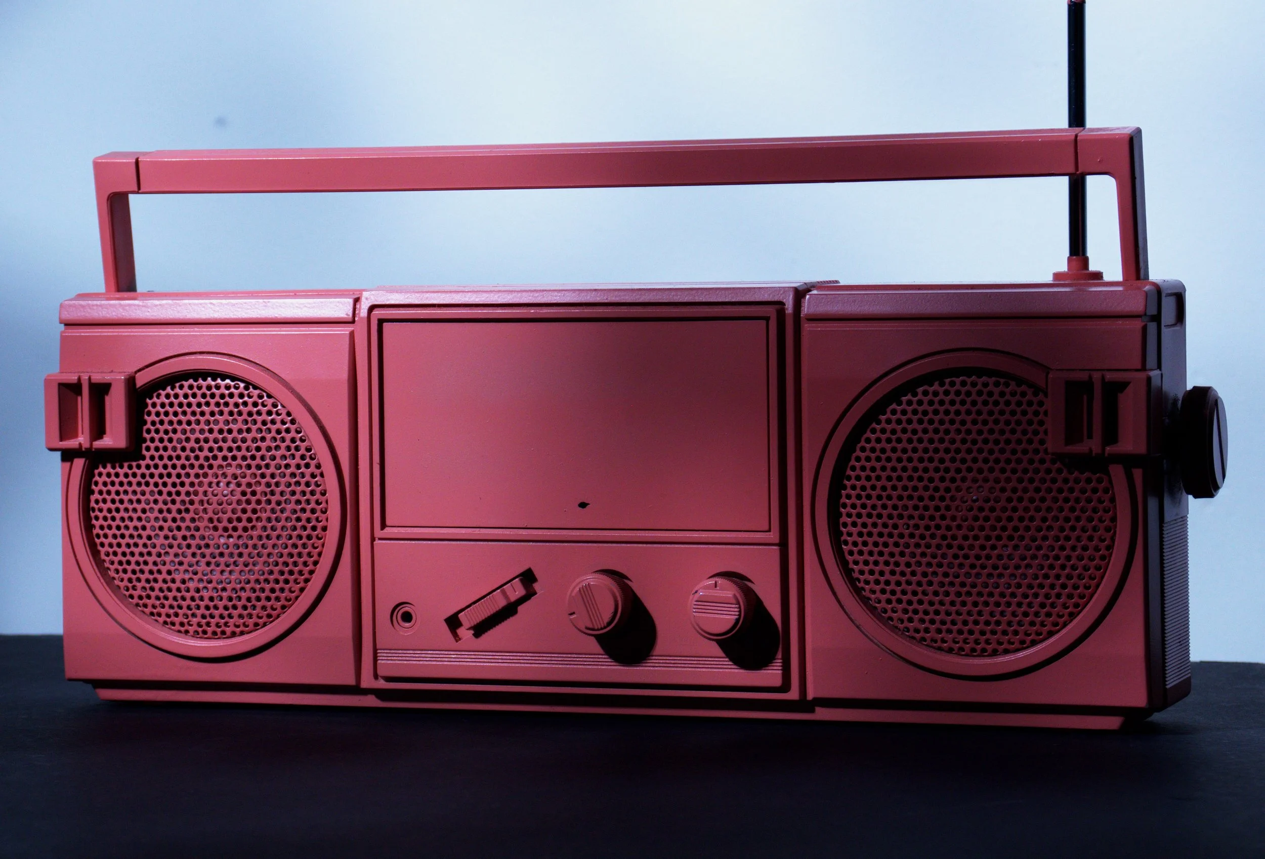 A pink portable stereo with two speakers, knobs, and a handle sitting on a dark surface.