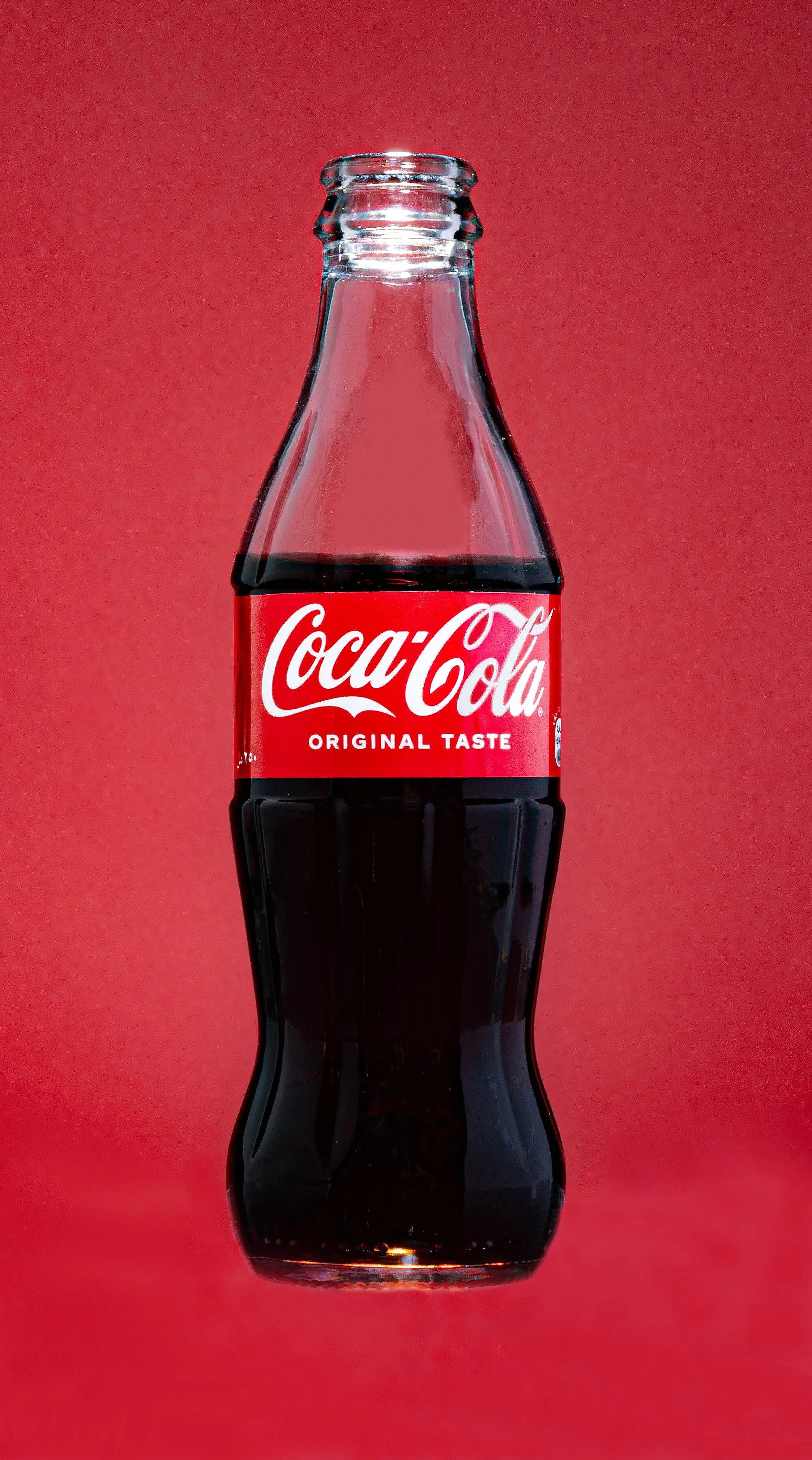 A glass bottle of Coca-Cola against a red background.