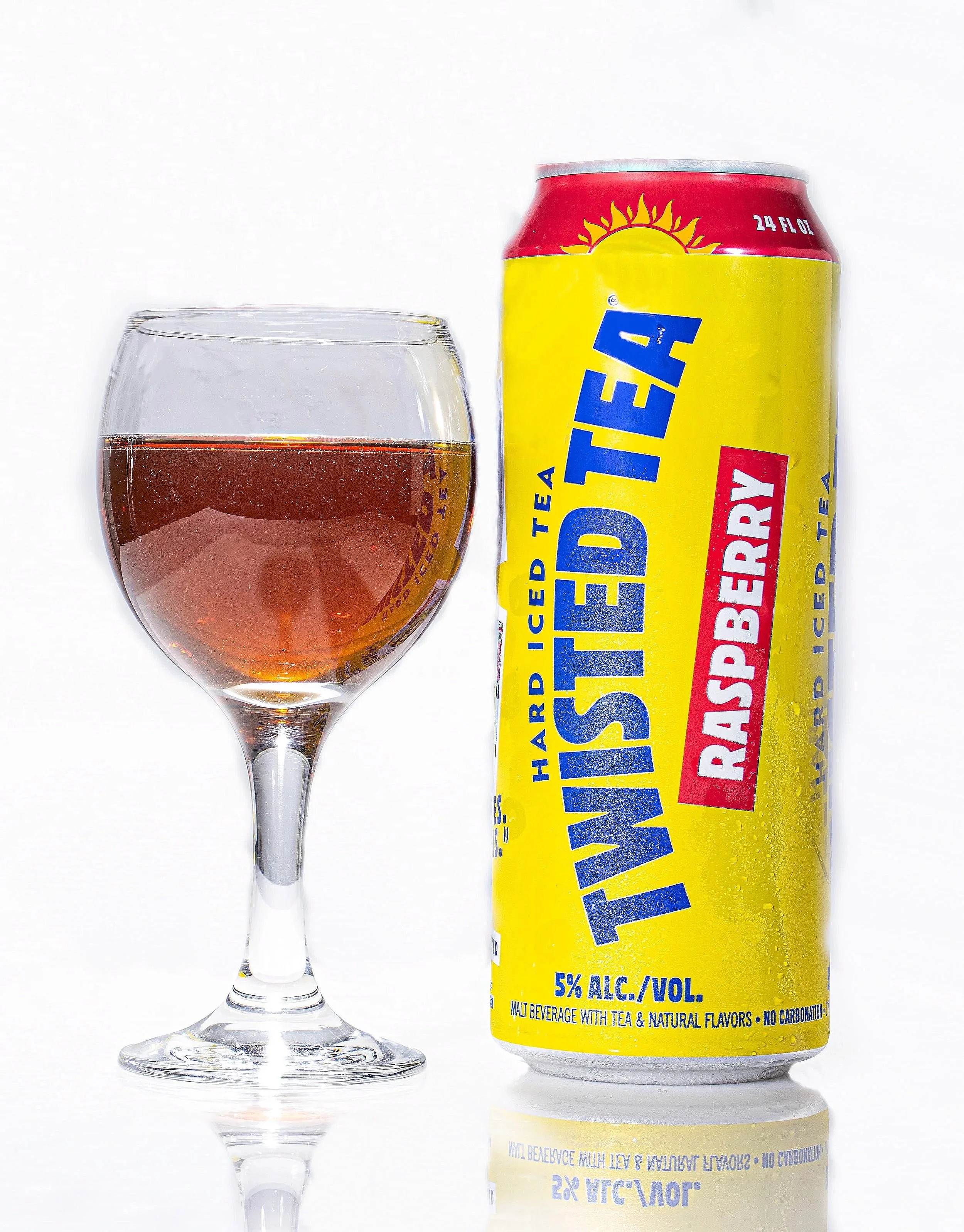 A glass of amber-colored iced tea next to a can of Lemonade Iced Tea with a yellow label and red top, on a white background.