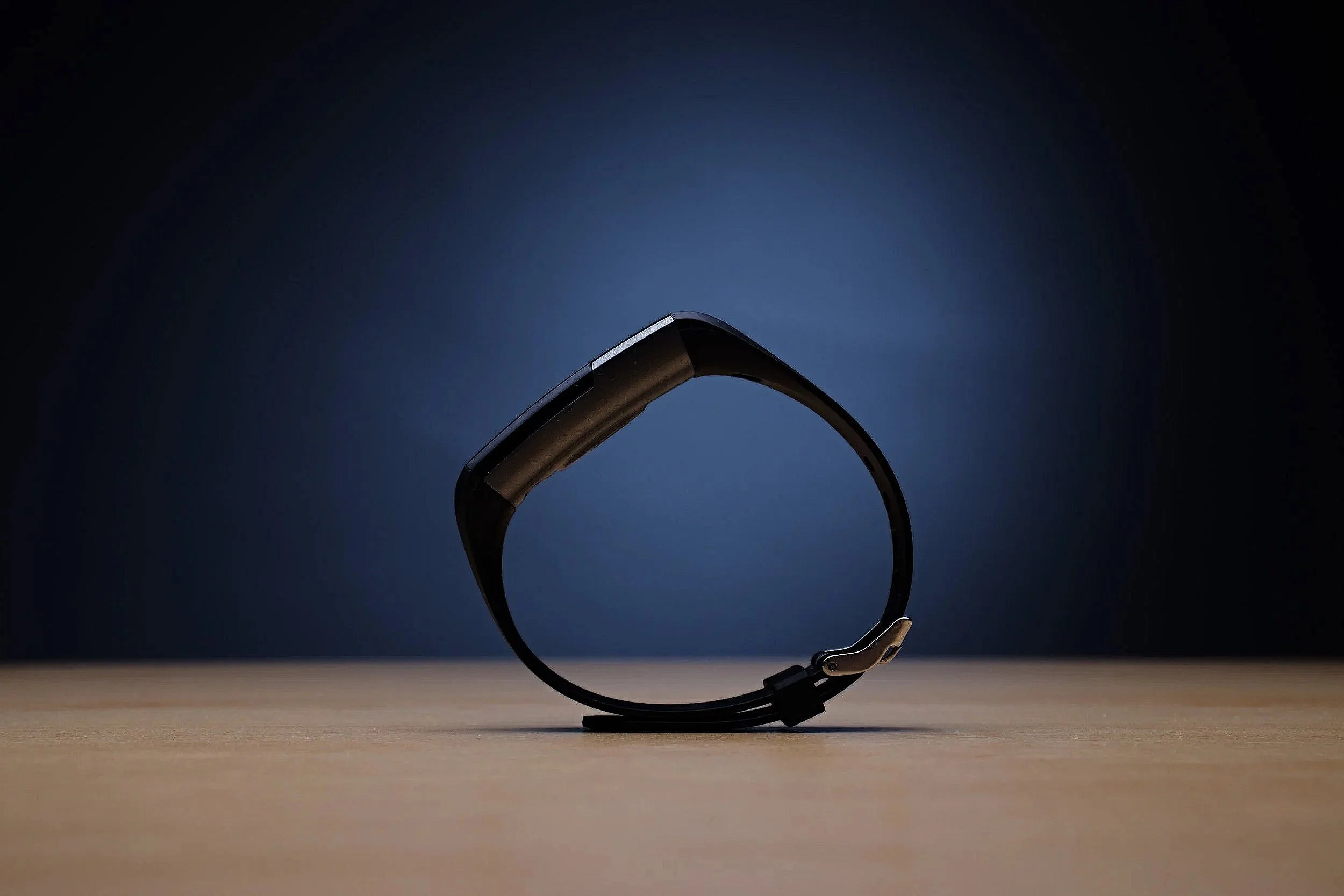 A sleek smartwatch with a curved display and a black band, standing upright on a flat surface against a dark background, illuminated by subtle lighting.