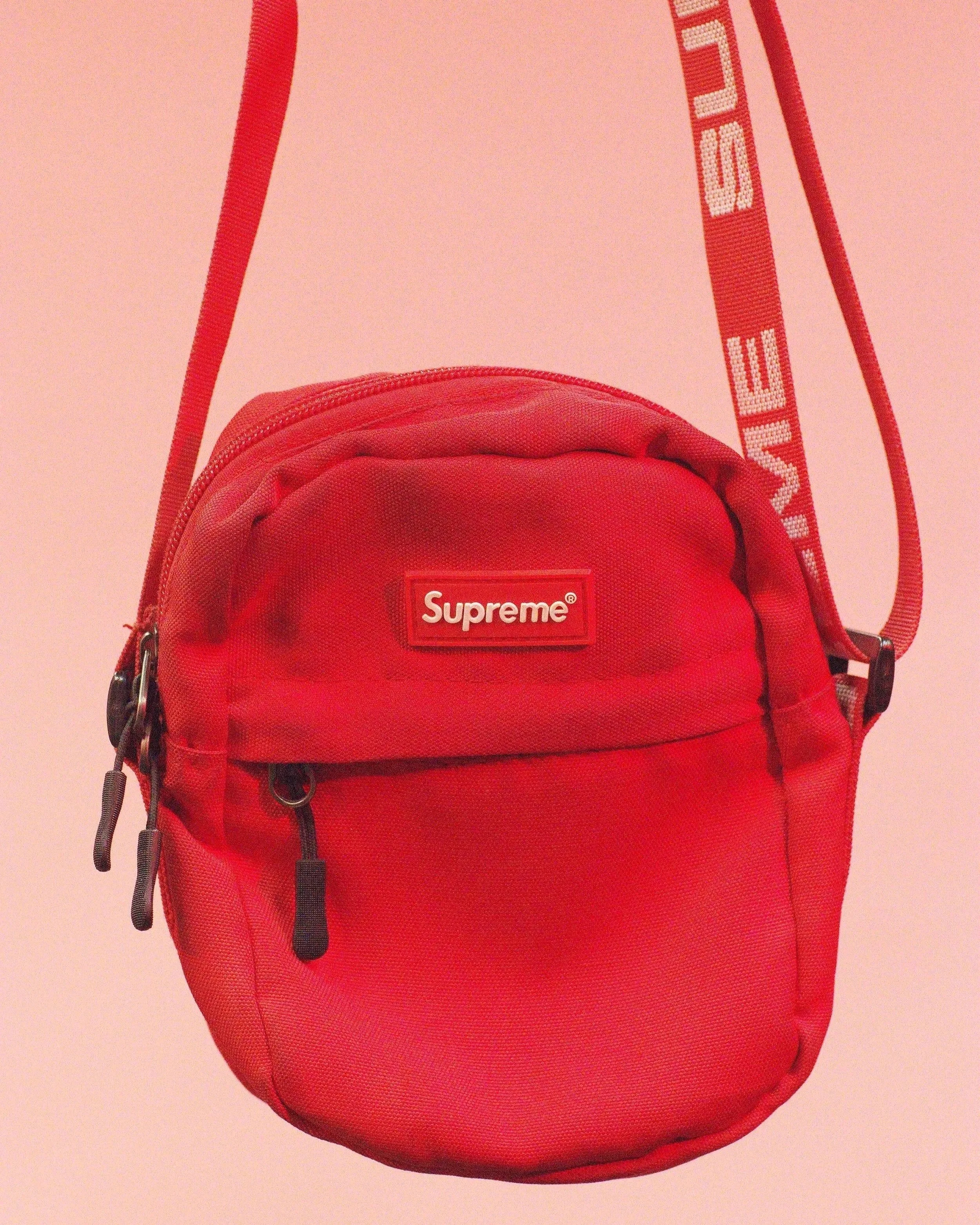 A red Supreme branded backpack with black zippers and straps, displayed against a plain light-colored background.