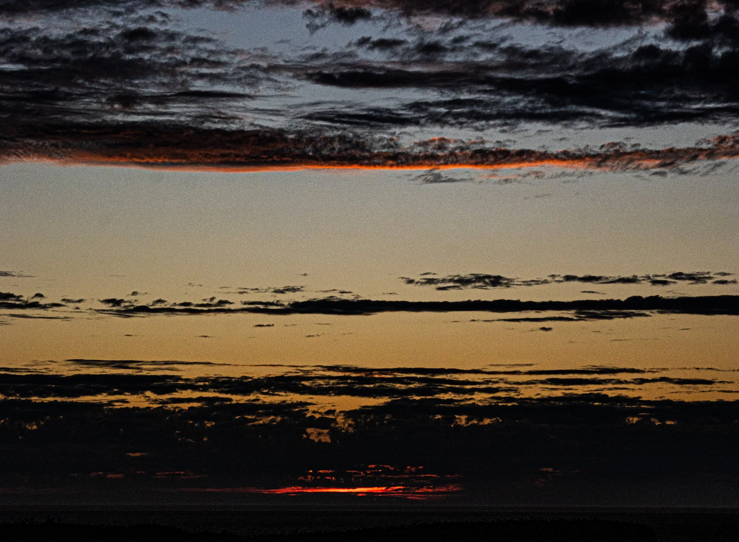 A sunset over a body of water with dark clouds in the sky and a hint of orange and red near the horizon.