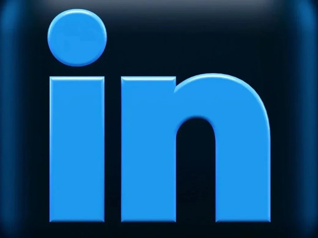 Close-up of the LinkedIn logo featuring a blue circle above the lowercase letters 'in' on a dark background.