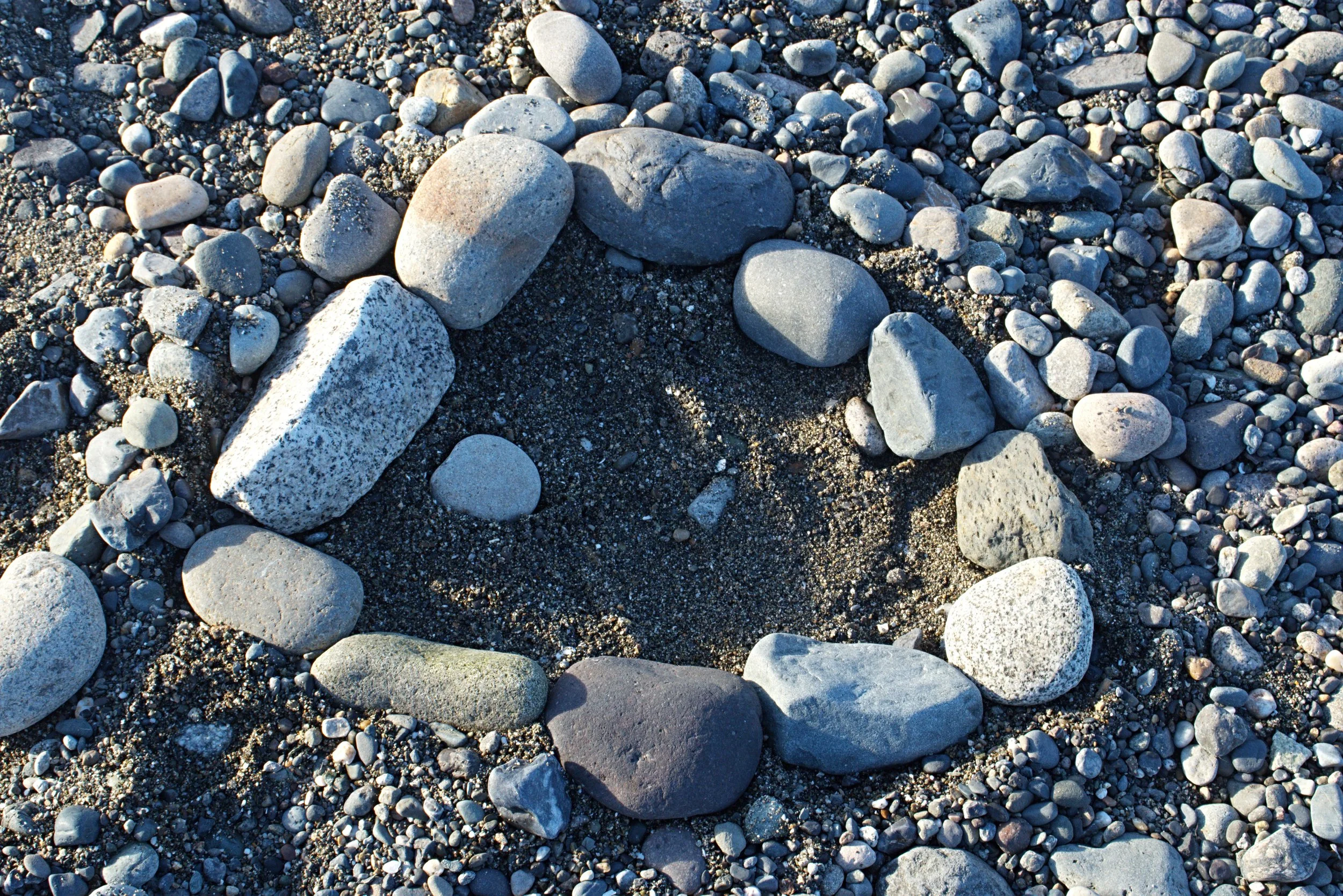 A close-up view of a gravelly beach with various sizes and colors of rocks and stones scattered across the sand.