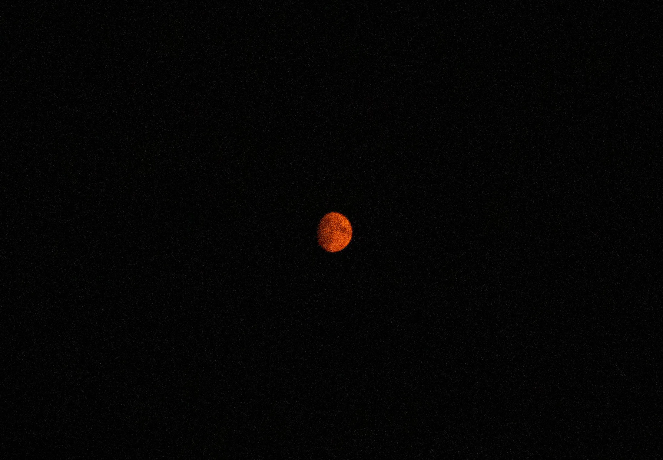 A reddish-orange circular object, likely a moon or planet, set against a black night sky with tiny stars.