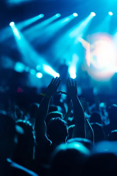 Crowd at a concert with a person dancing and hands raised, illuminated by blue stage lights.